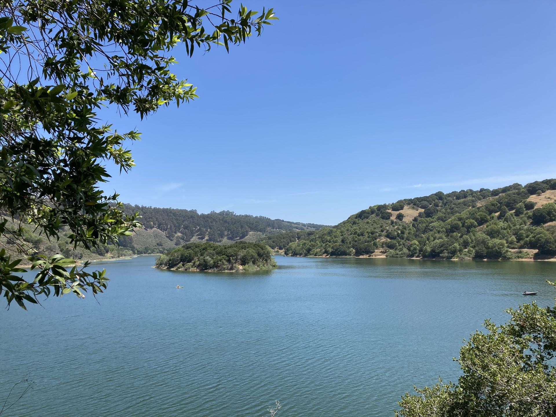Sunny view of a calm lake with a small island and green hills.