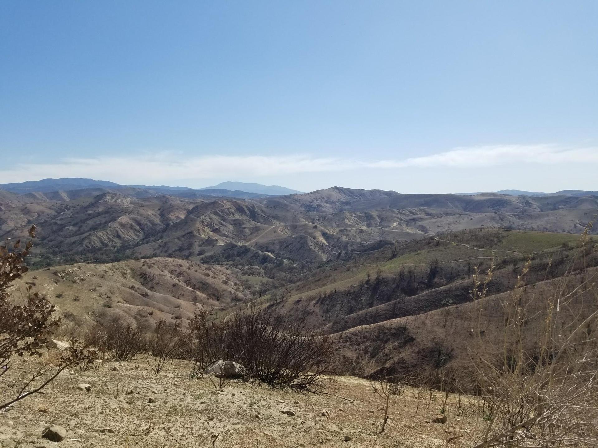 Vast, dry mountainous landscape under a clear blue sky with rolling hills.