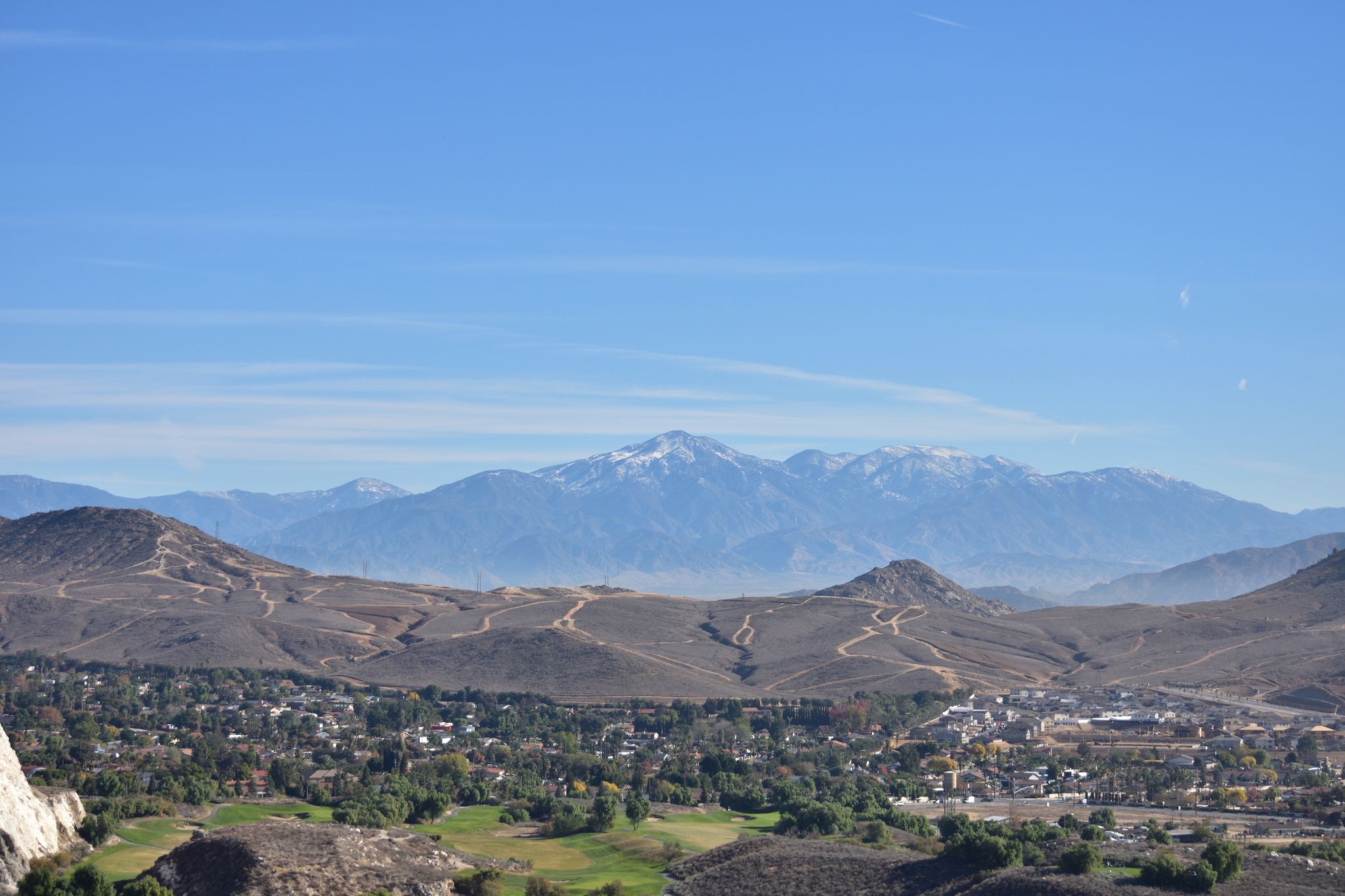 Bright daylight illuminates a town in a valley, dry hills, and distant snow-capped mountains. - West Condominium Road loop