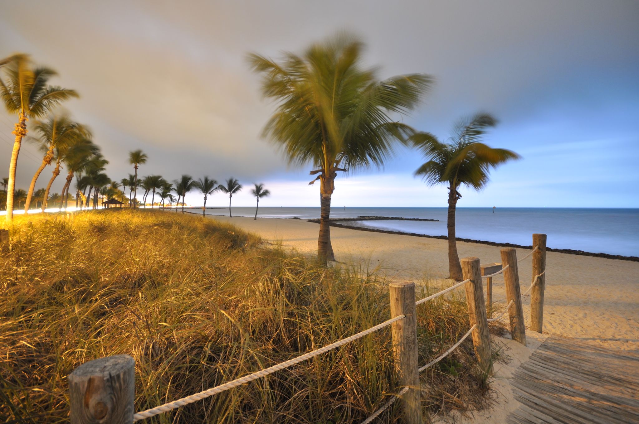 Palm trees on a sandy beach at dusk, with a boardwalk and ocean. - Historic House in Key West – Smathers Beach loop from Key West