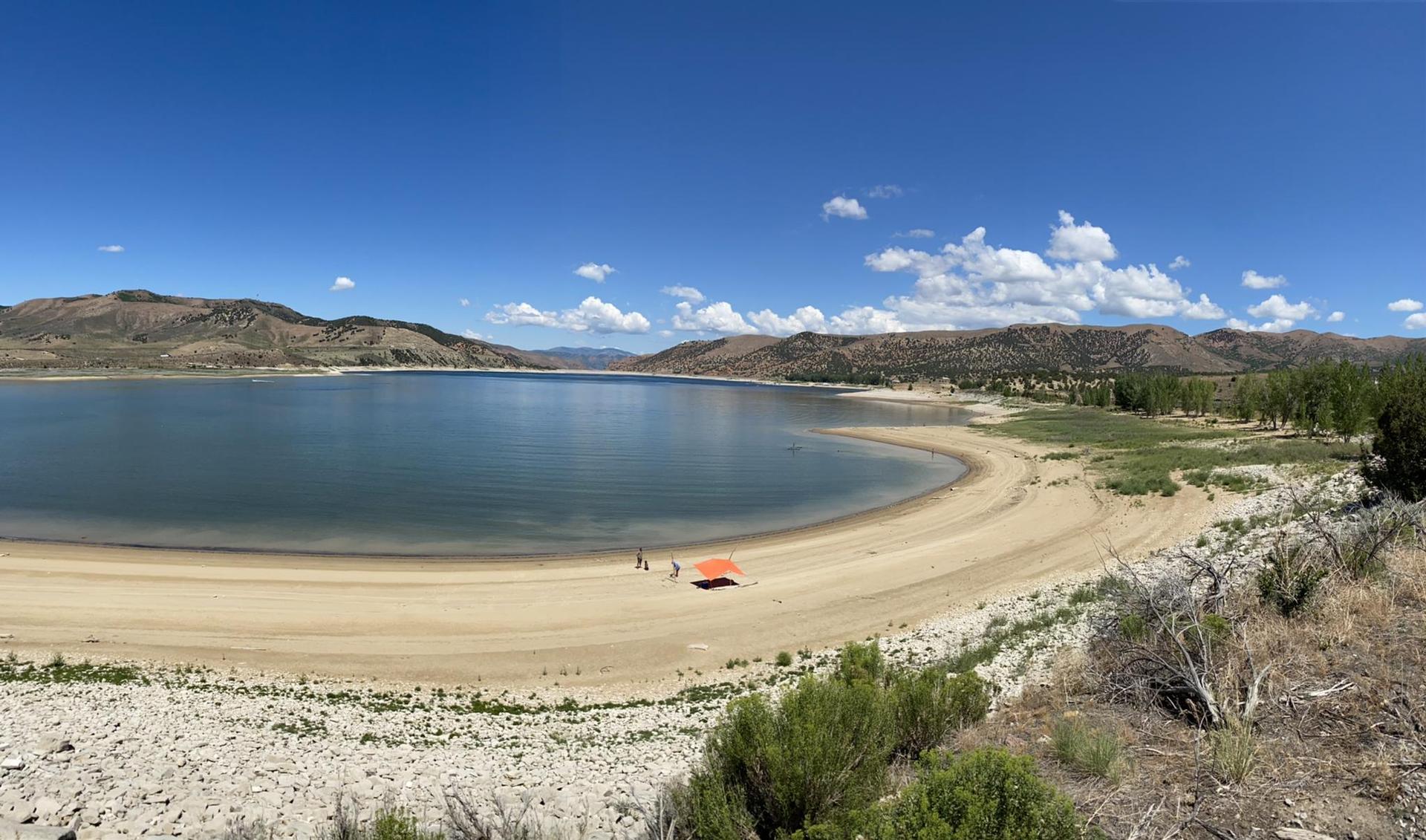 Panoramic view of a large lake, sandy beach, distant mountains, and blue sky.