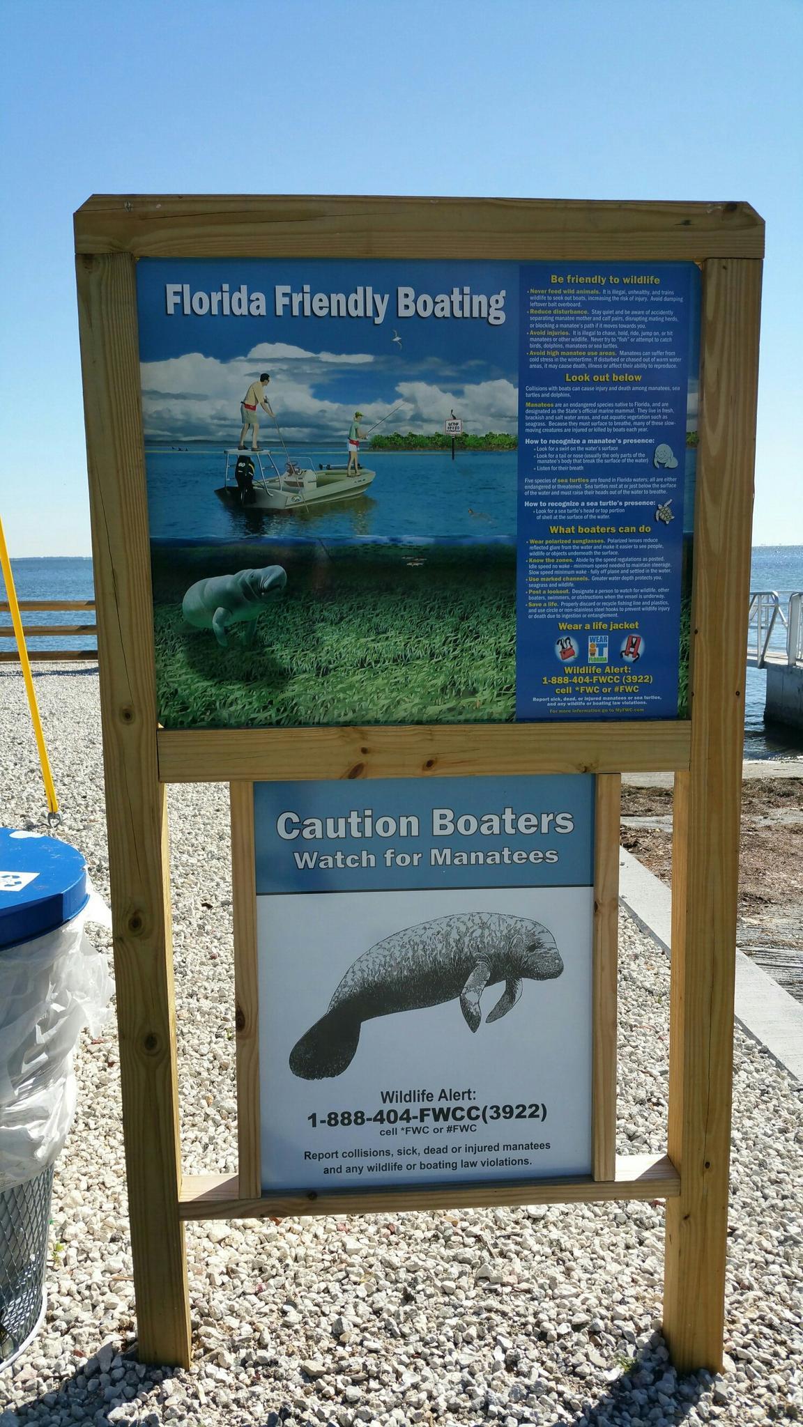 Wooden sign with boating and manatee information panels under bright sunlight.
