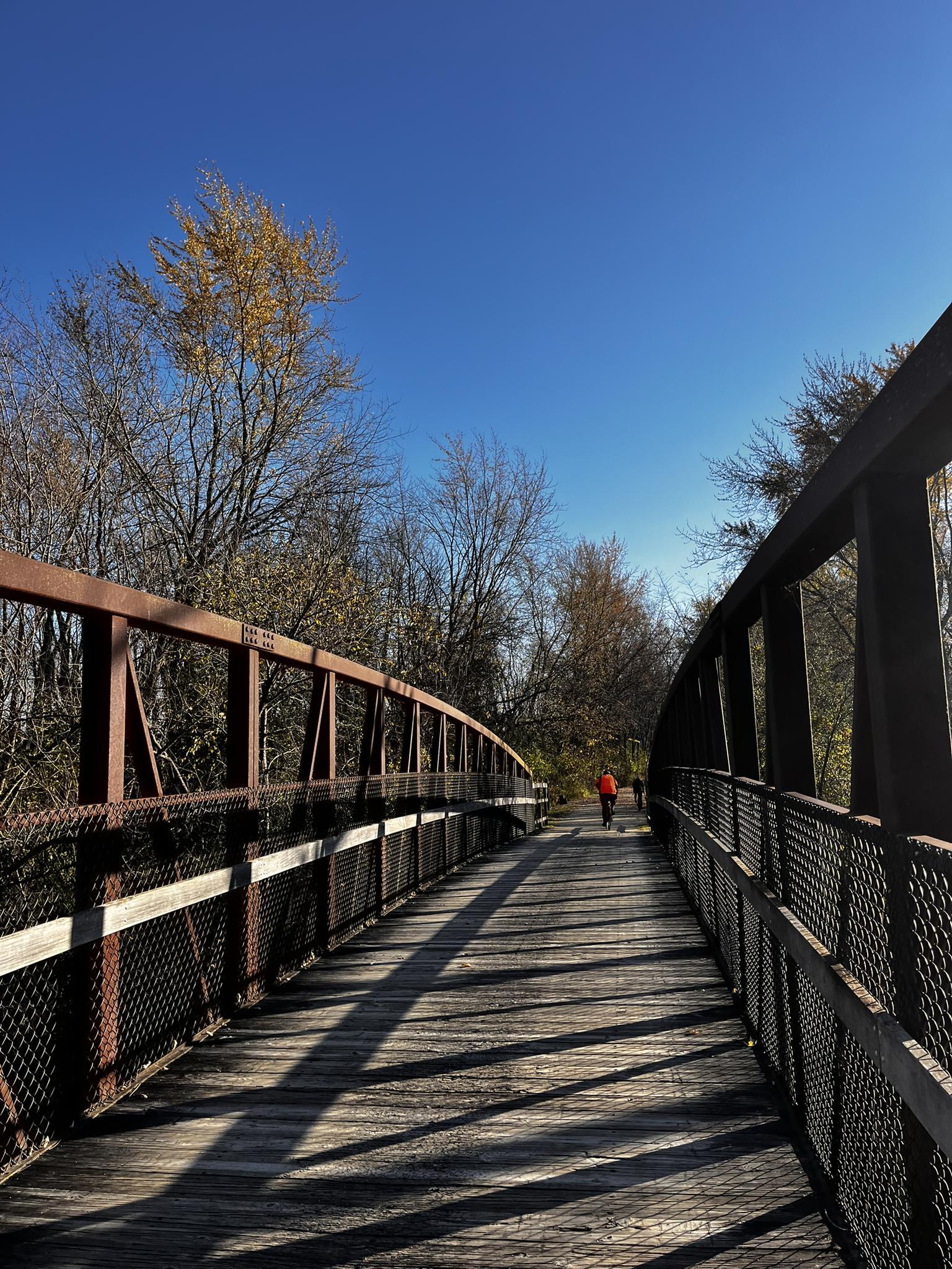 Long wooden and metal bridge with a person walking, sunny autumn day.