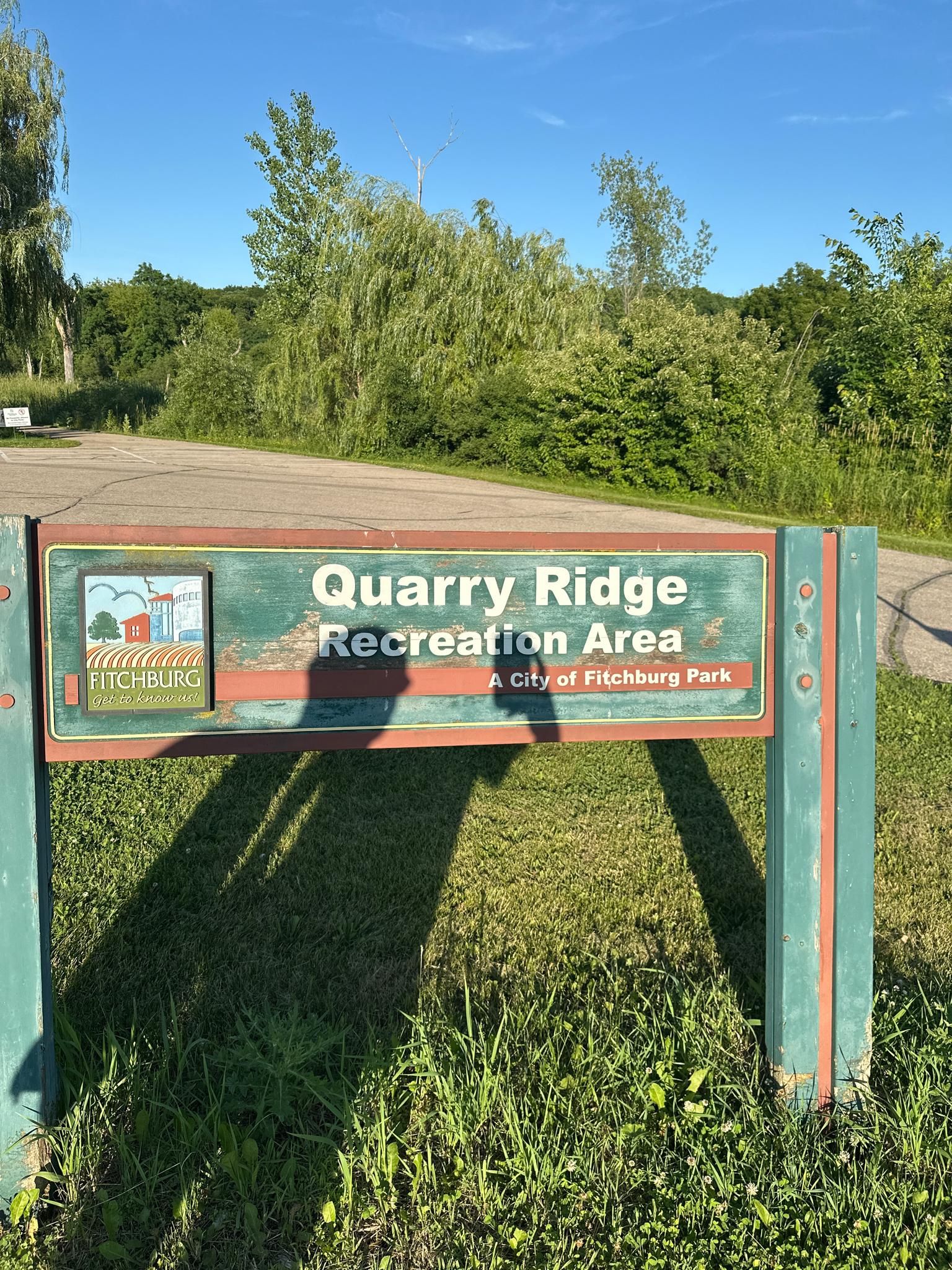 A wooden sign with green and brown trim, surrounded by bright green grass. - Goose Lake – Quarry Ridge Recreation Area loop from Mount Horeb