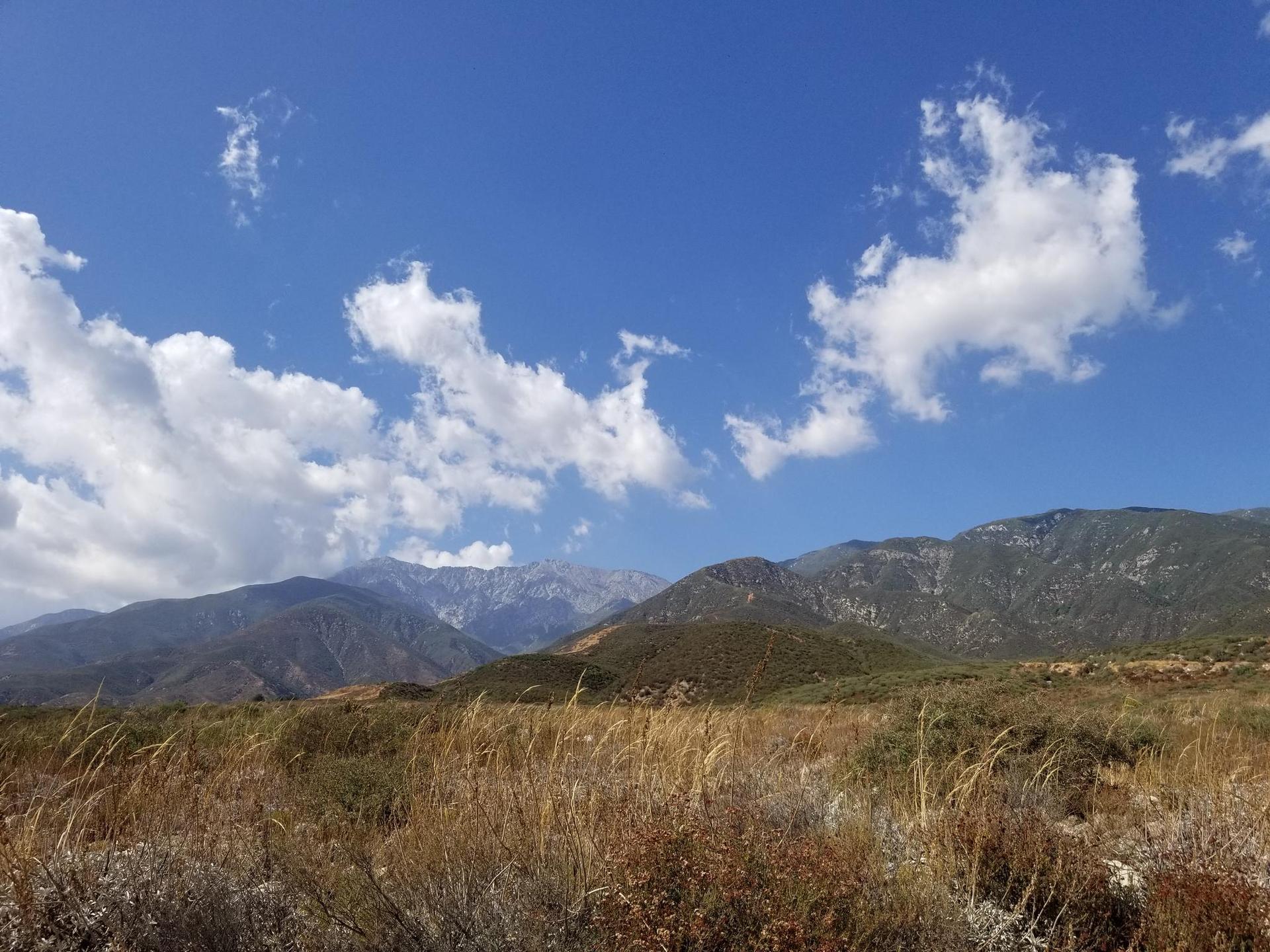Expansive view of dry grassy hills and distant mountains under a blue sky.