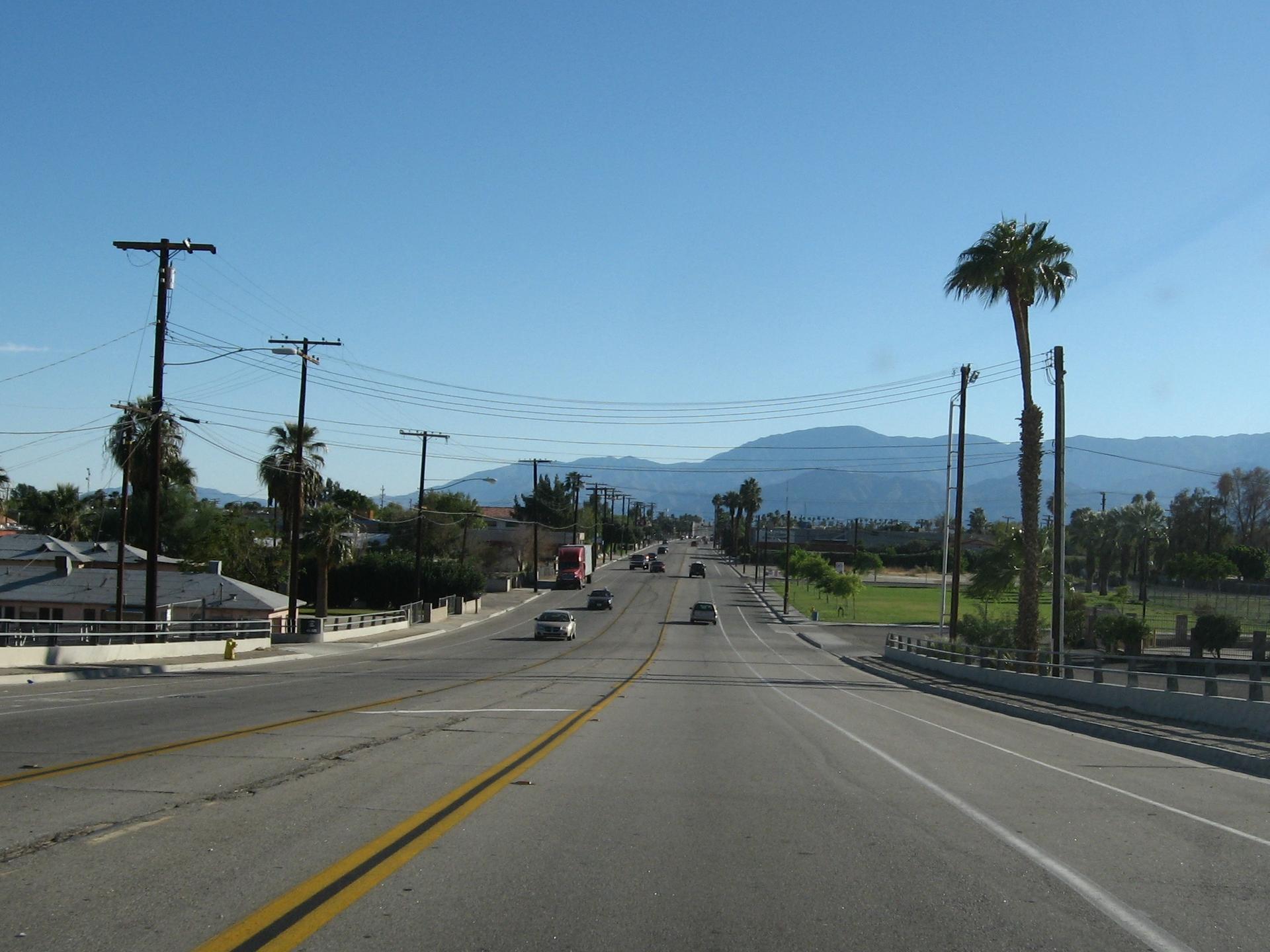 A wide road with cars, power lines, and mountains under a clear sky.