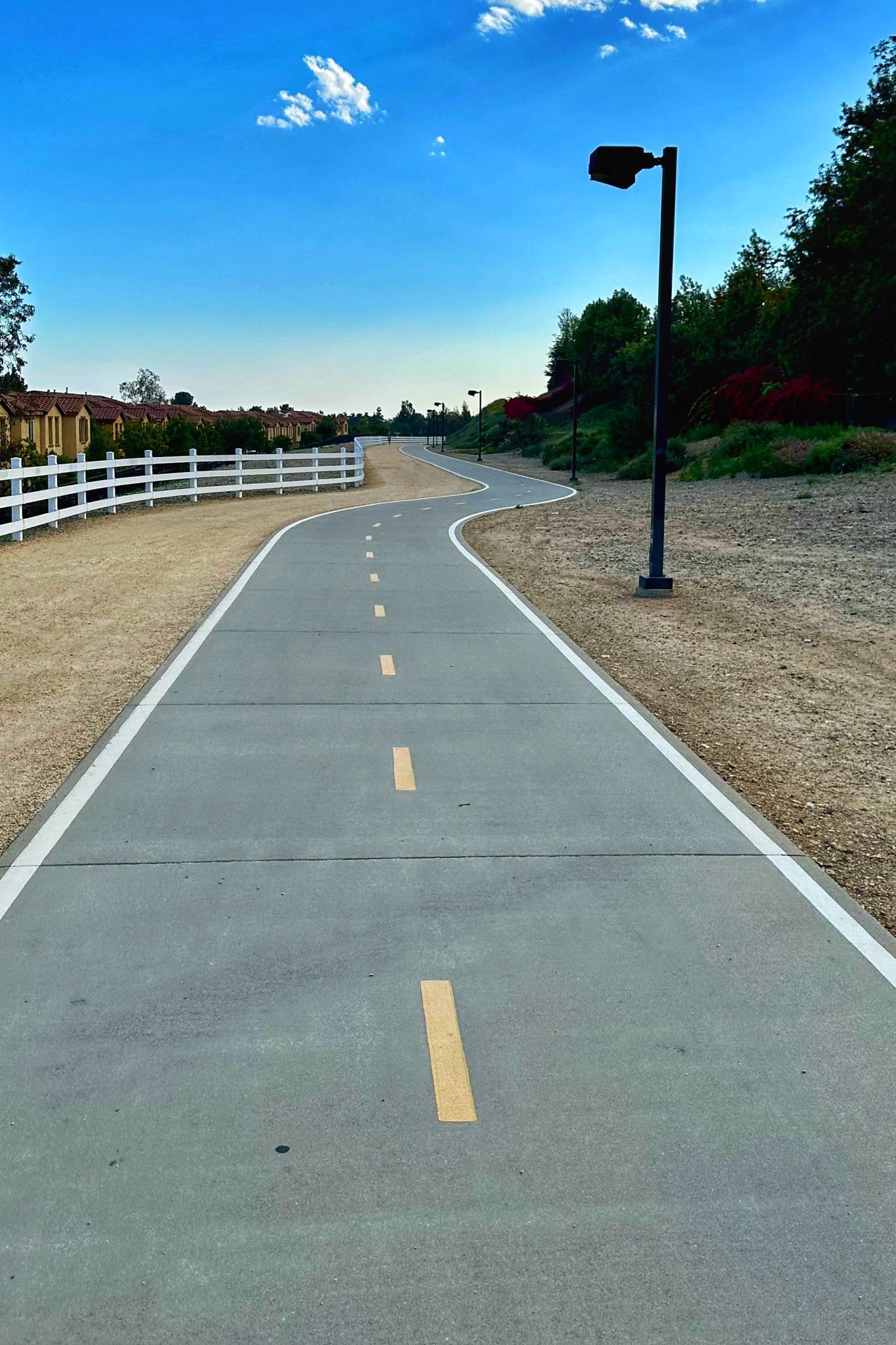 A winding paved path with yellow lines under a bright blue sky.