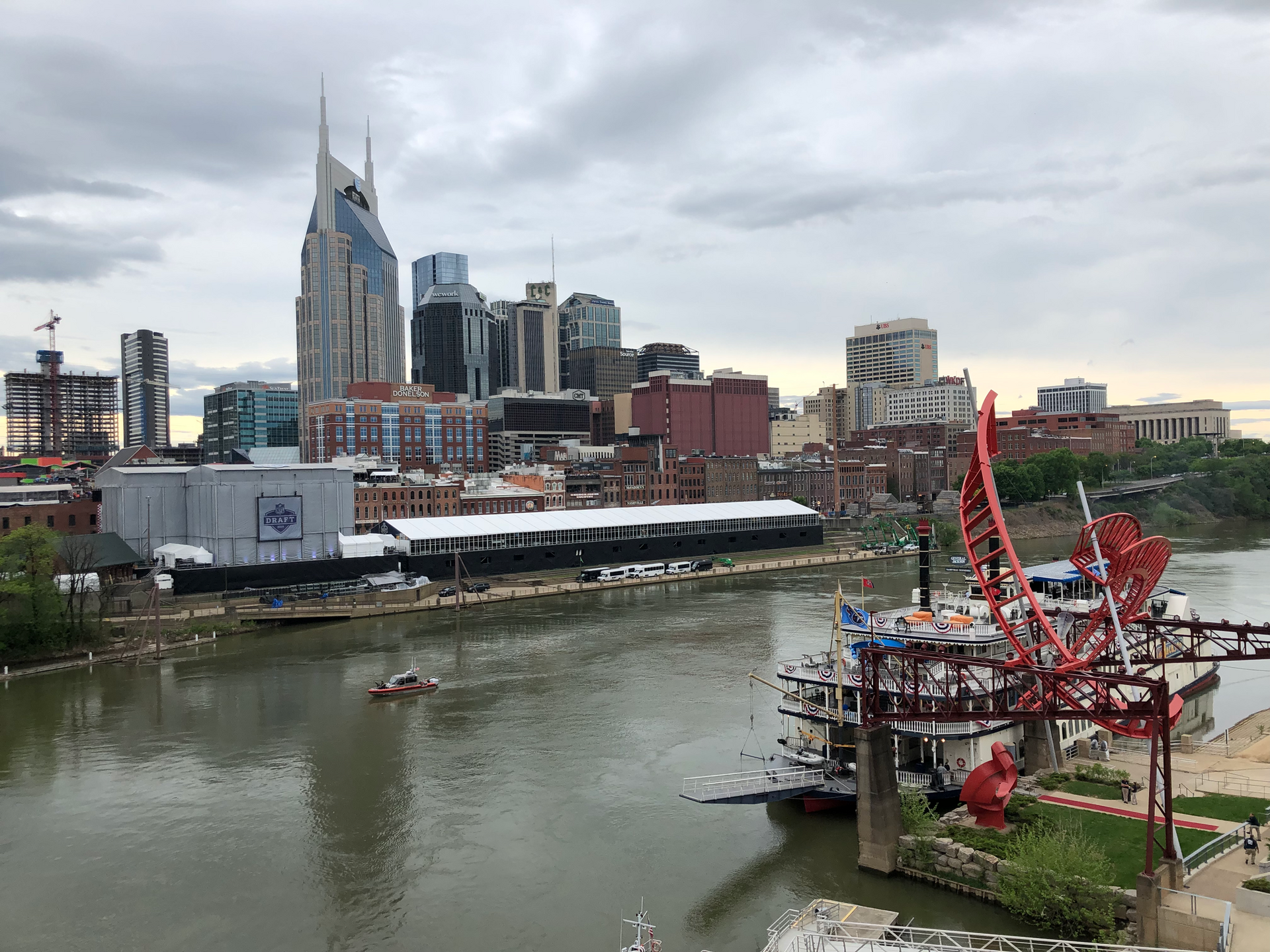 Overcast city skyline with a wide river, boats, and modern buildings.