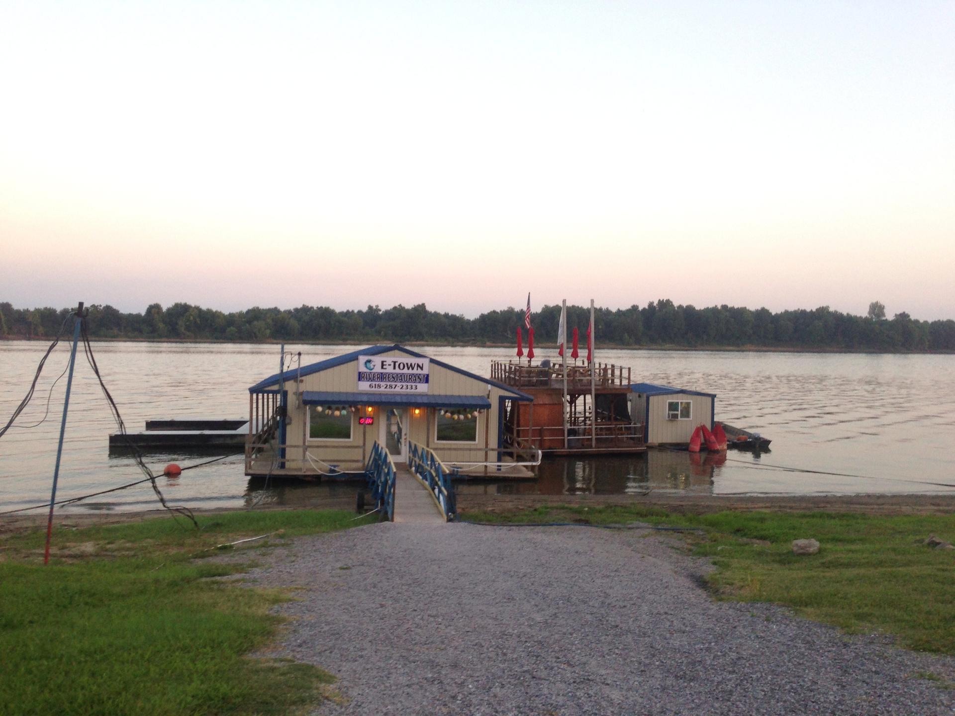 A floating building on a wide river at dusk, with a gravel path.