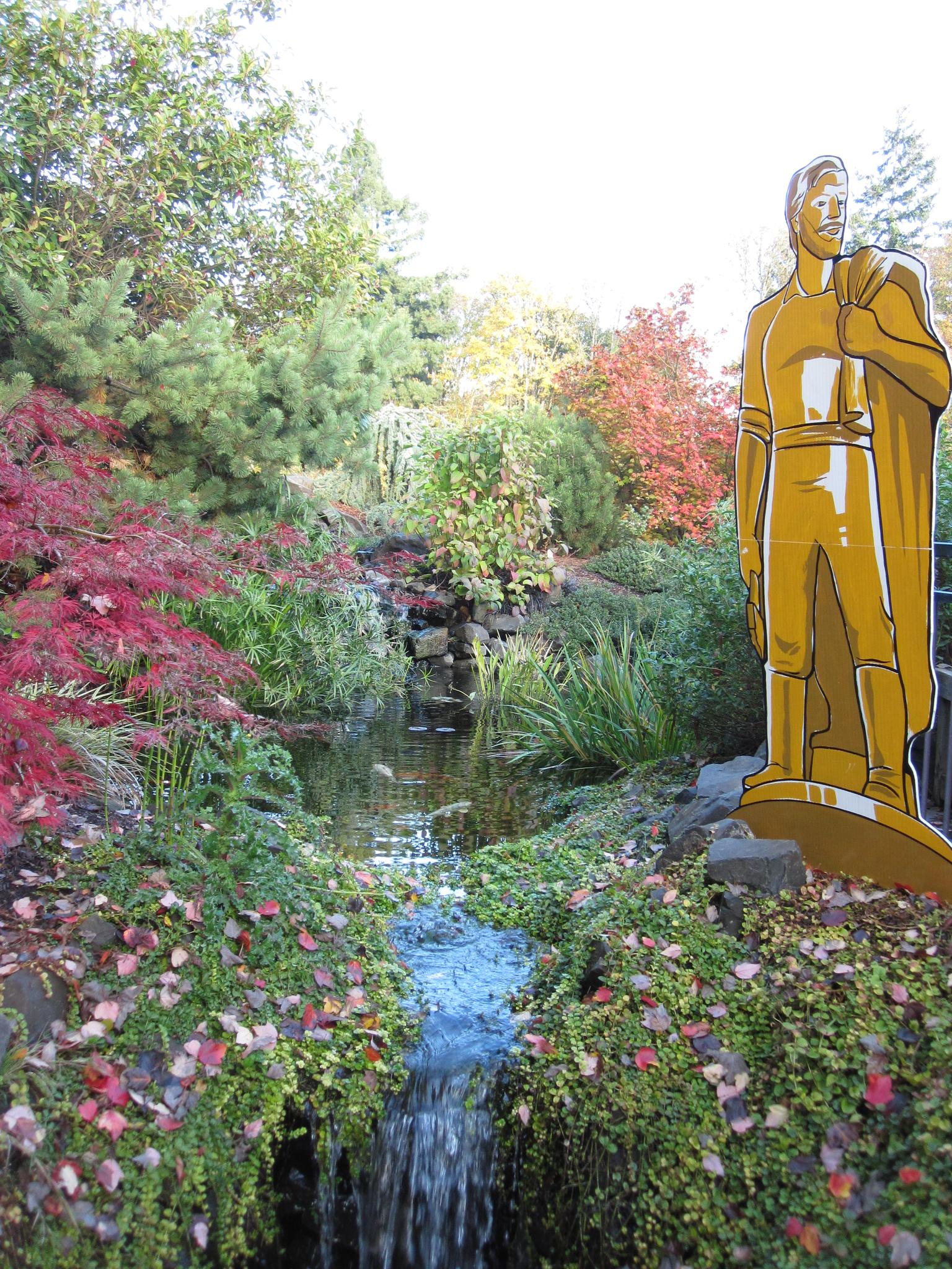 Golden statue stands beside a small waterfall in a vibrant, colorful garden.