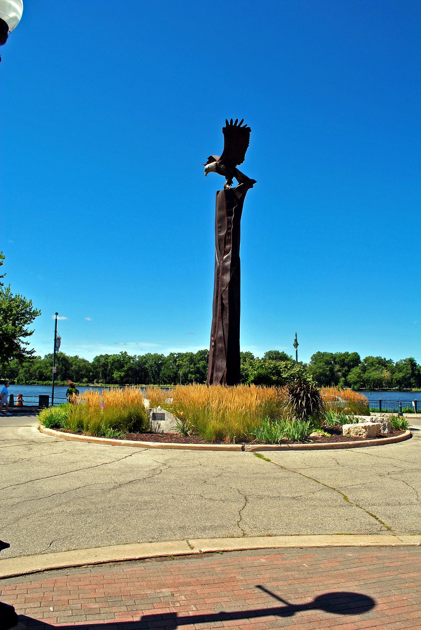 A large eagle statue on a tall pedestal under a clear blue sky.