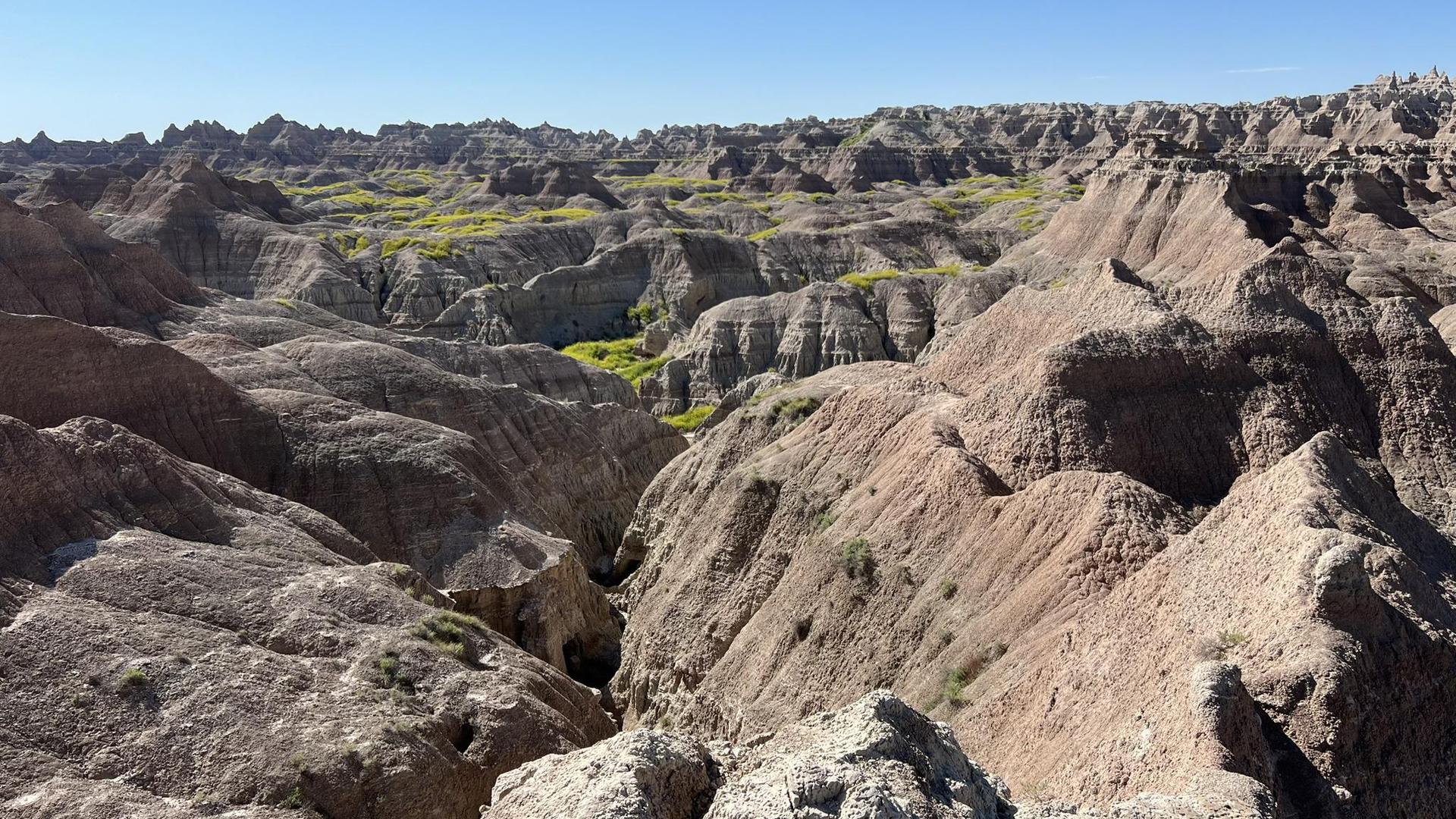Expansive view of eroded badlands formations with green vegetation in valleys.