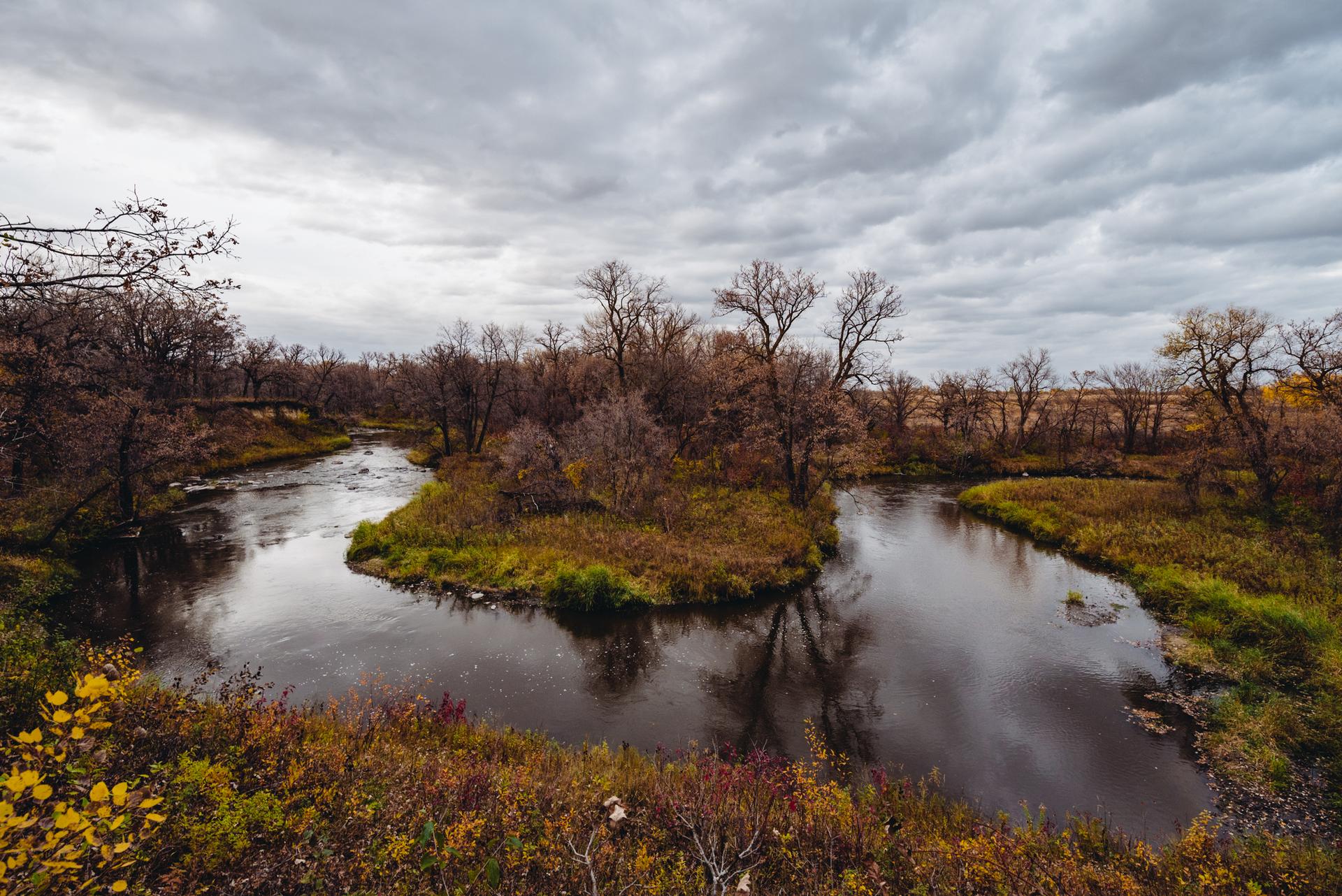 A river splits around an island, surrounded by autumn trees under a cloudy sky.