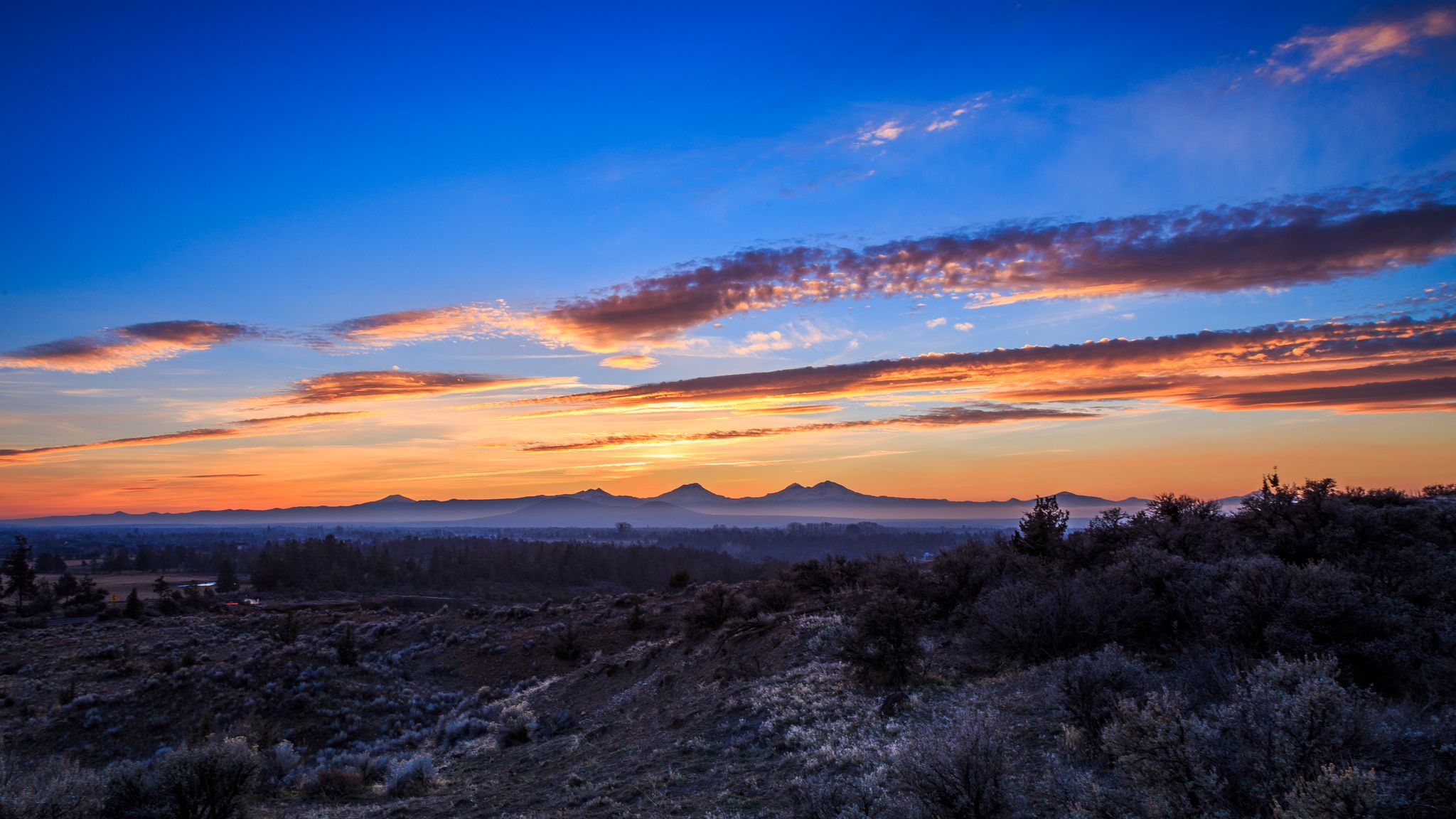 Vibrant sunset over a distant mountain range and a vast, shrubby landscape. - Dry Canyon Trail – Dry Canyon Wildlife loop from Redmond High School
