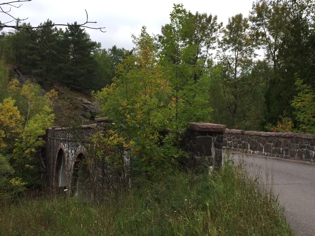 Old stone arch bridge surrounded by green and yellow trees on an overcast day. - Seven Bridges Road loop from Lakeside-Lester Park