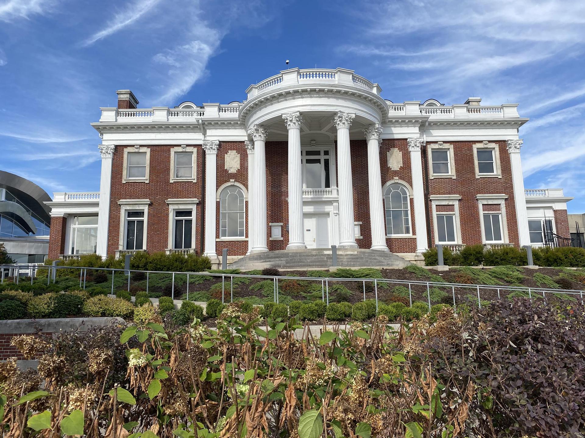 Grand brick building with white columns and portico under a blue sky.