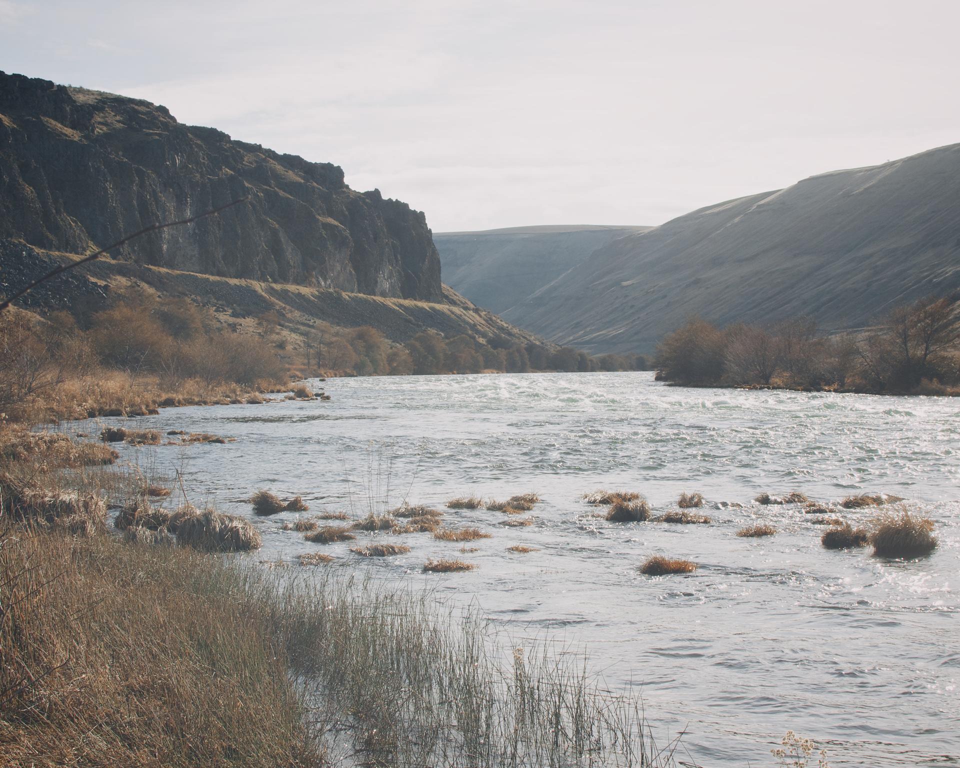 A wide river with rocky banks flows through a sunny, hazy canyon.