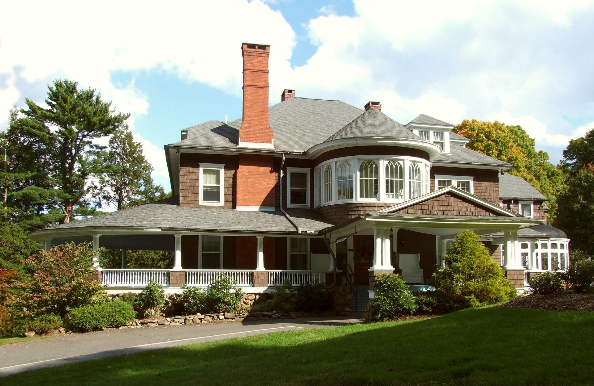 A grand, historic brown house with a large porch and bay window, sunny day.