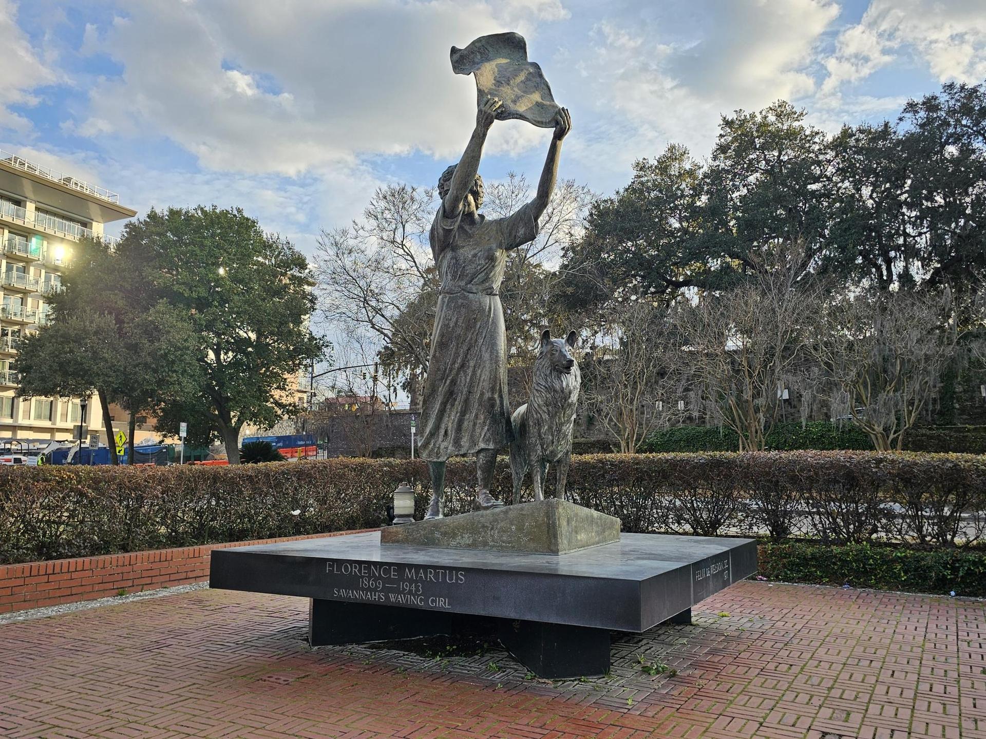 Bronze statue of a woman and dog in a park on a sunny day.