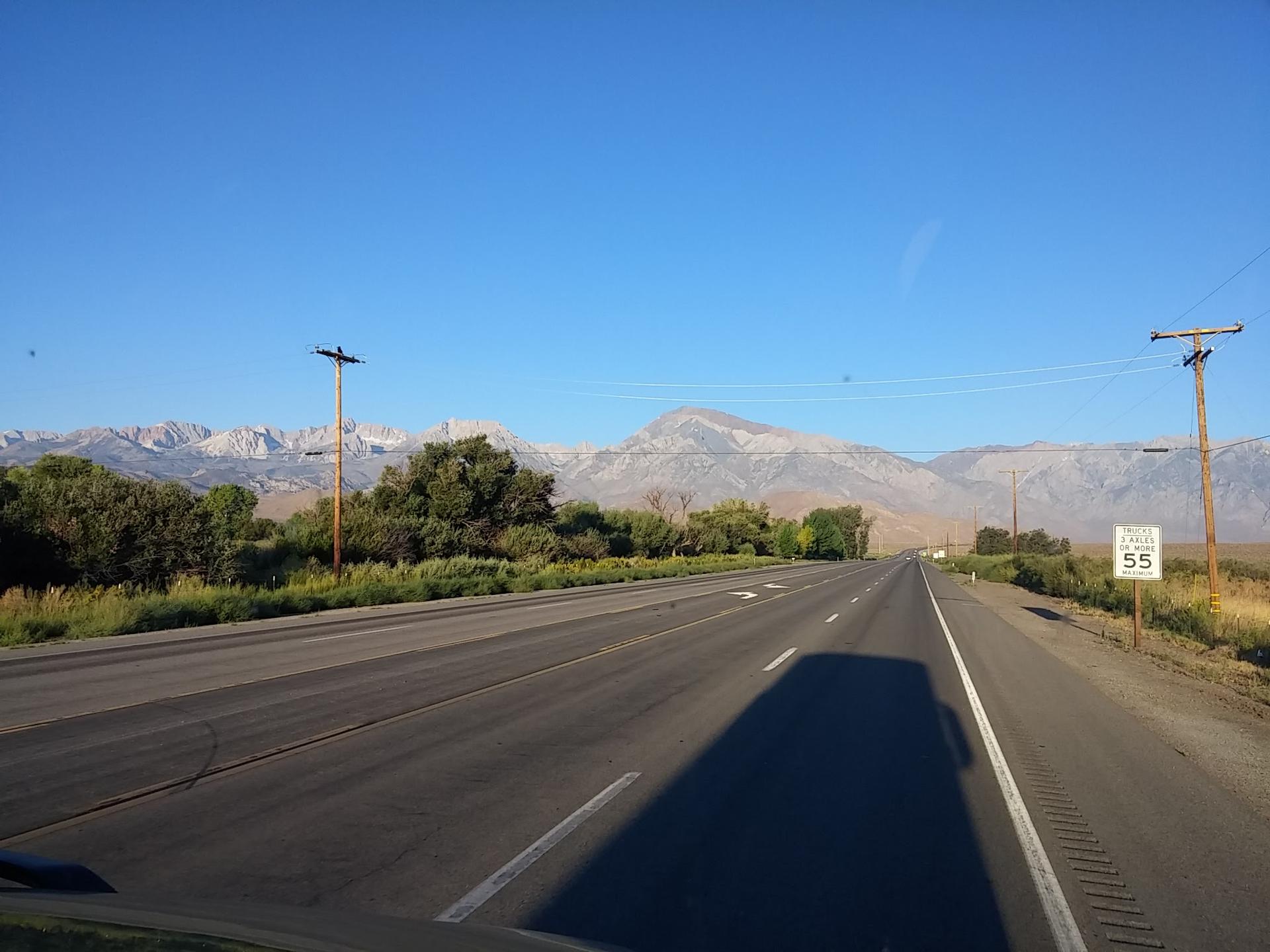 Empty highway stretching towards distant mountains under a clear blue sky.
