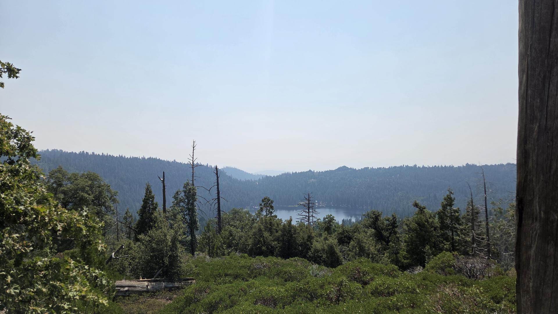 Panoramic view of a lake nestled in a forested valley under a hazy sky.