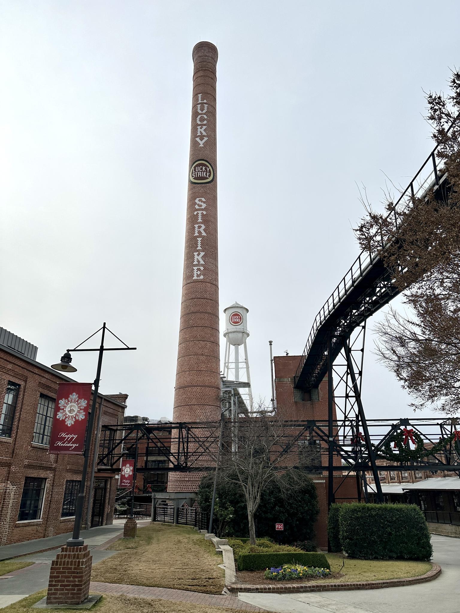 Tall brick smokestack with text, water tower, and industrial buildings on overcast day.