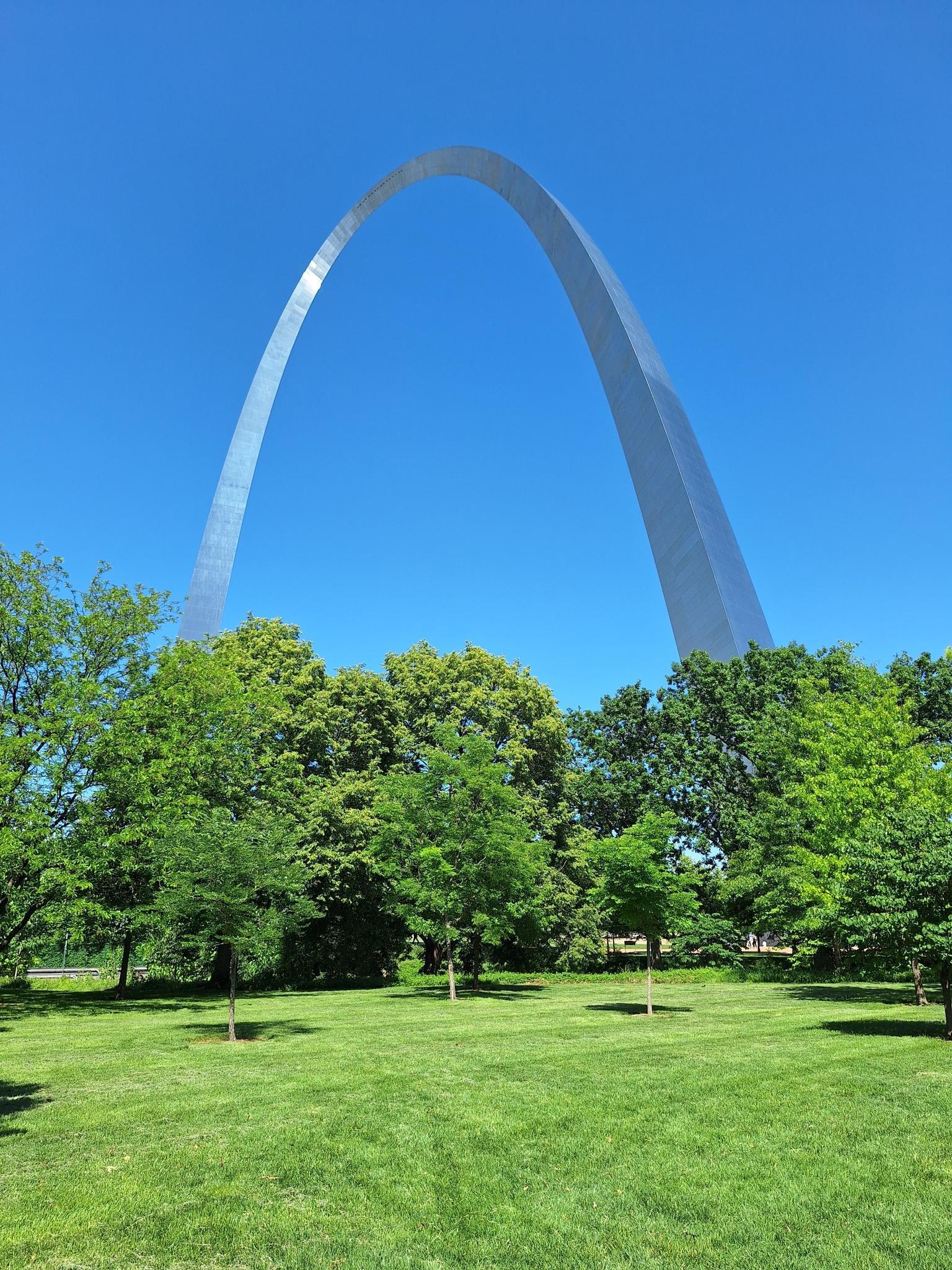 Tall arch rising above lush green trees and a vibrant grassy park.