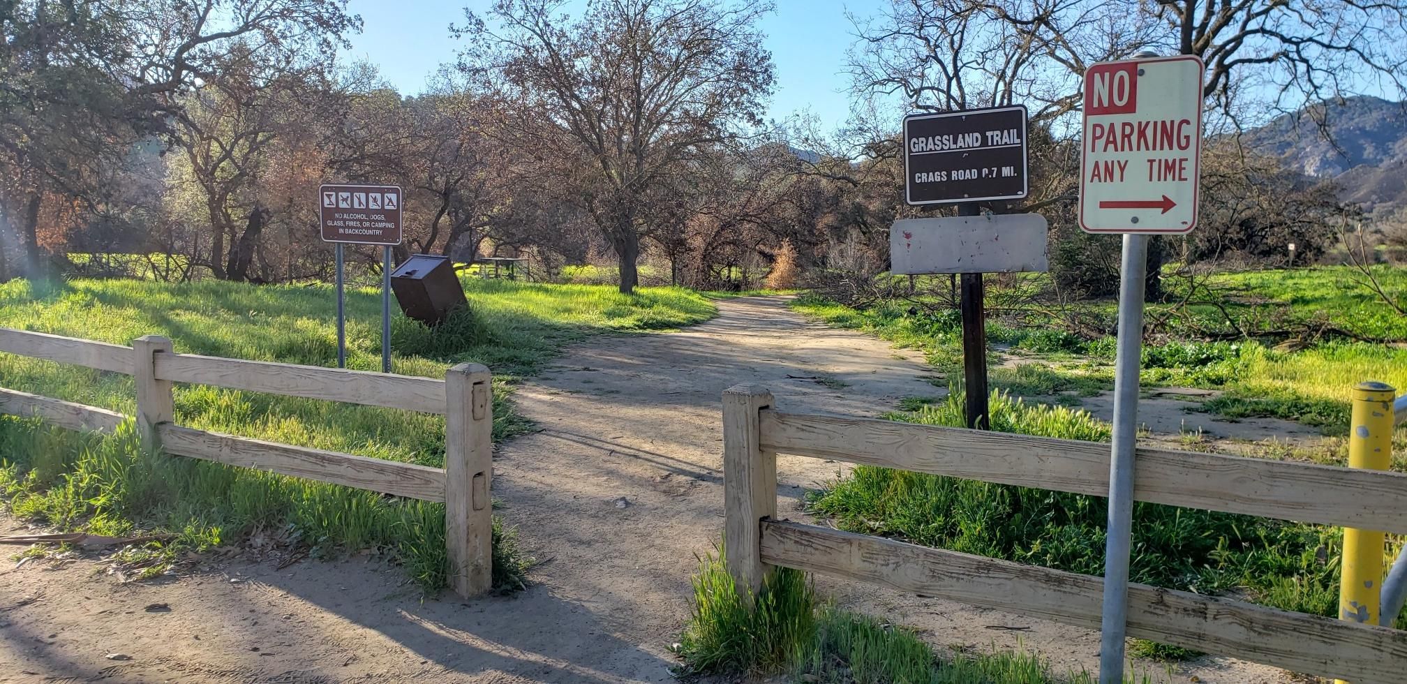 Sunny trail entrance with wooden fence and multiple signs. - Grasslands Trailhead – Las Virgenes Fire Road Trail loop from Las Virgenes MWD Open Space