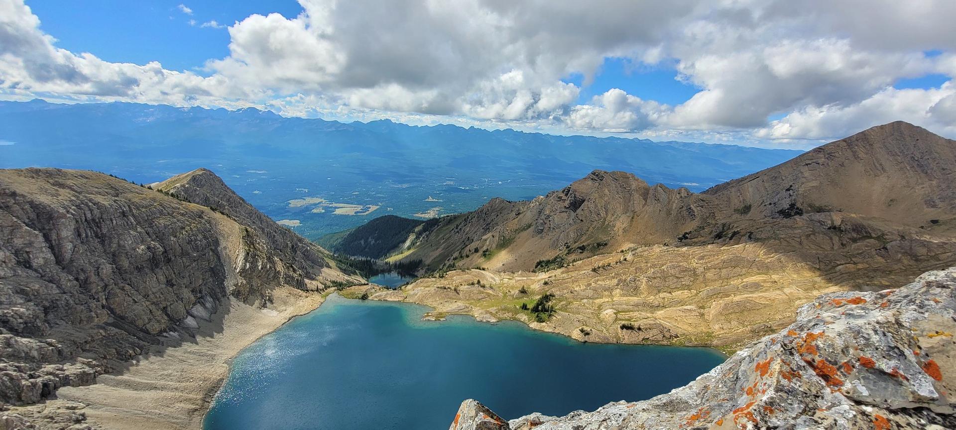 Panoramic view of a bright blue mountain lake surrounded by rocky peaks under a cloudy sky.