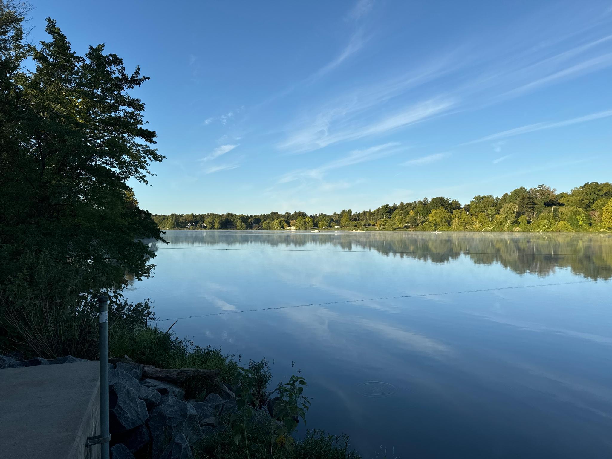 A calm lake reflects a bright blue sky with wispy clouds.