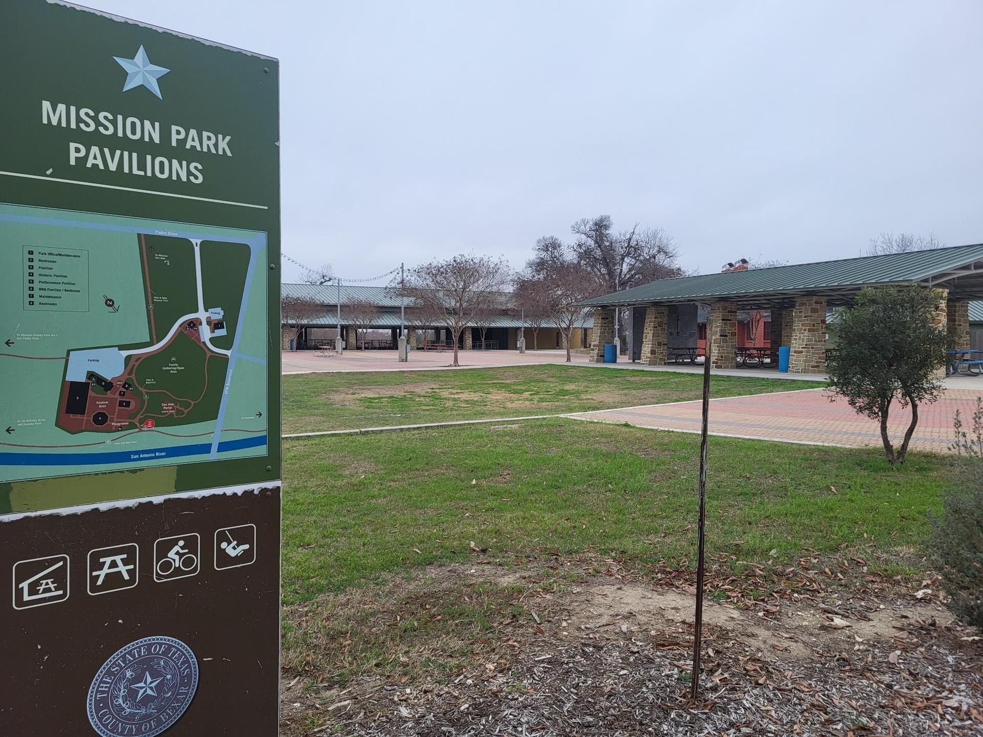 Park sign in foreground with pavilions and green lawn behind.