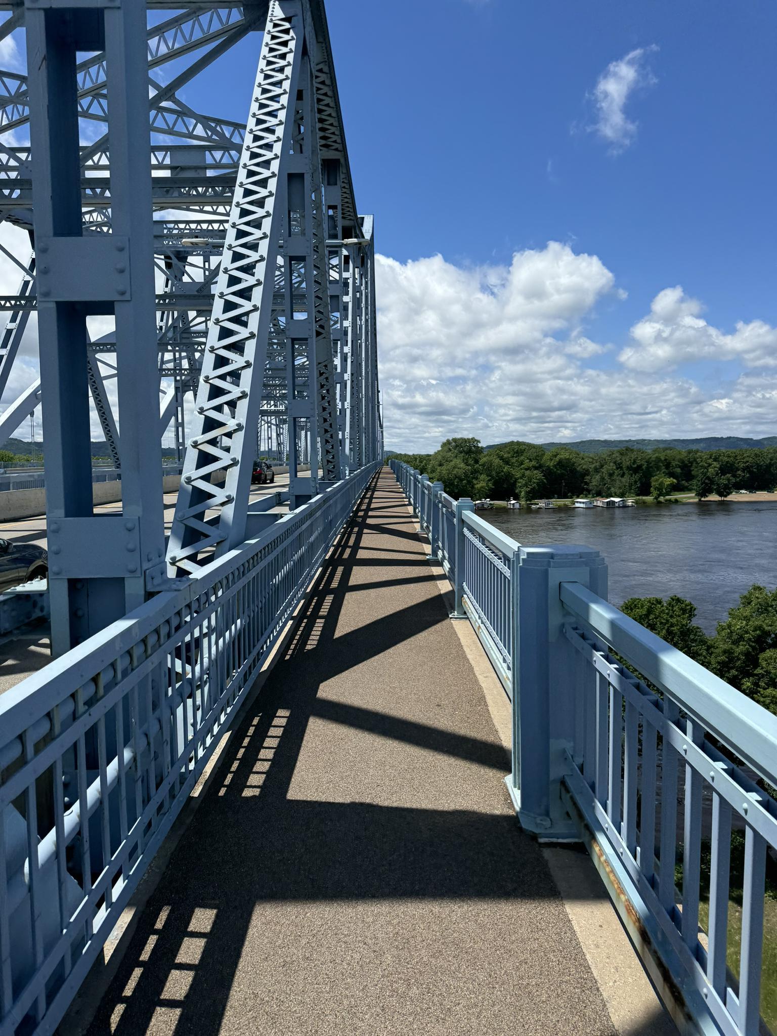 A pedestrian walkway on a blue truss bridge overlooks a wide river.