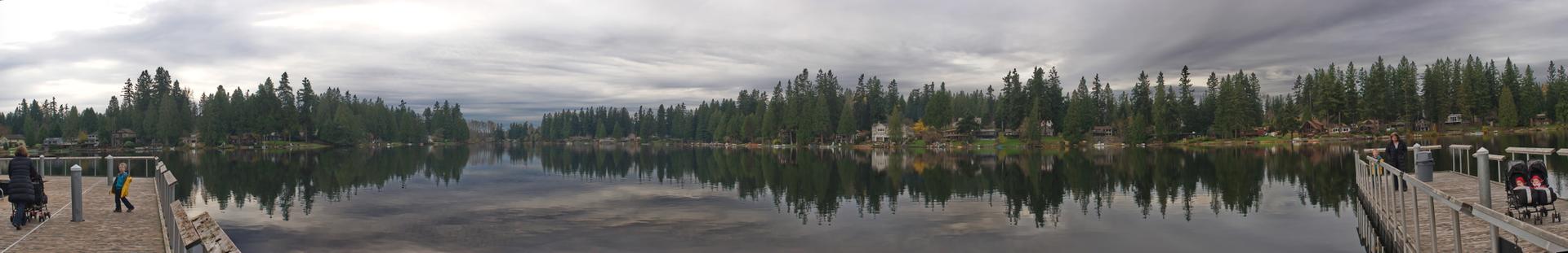 Panoramic view of a calm lake, docks, and dense forests under cloudy sky.