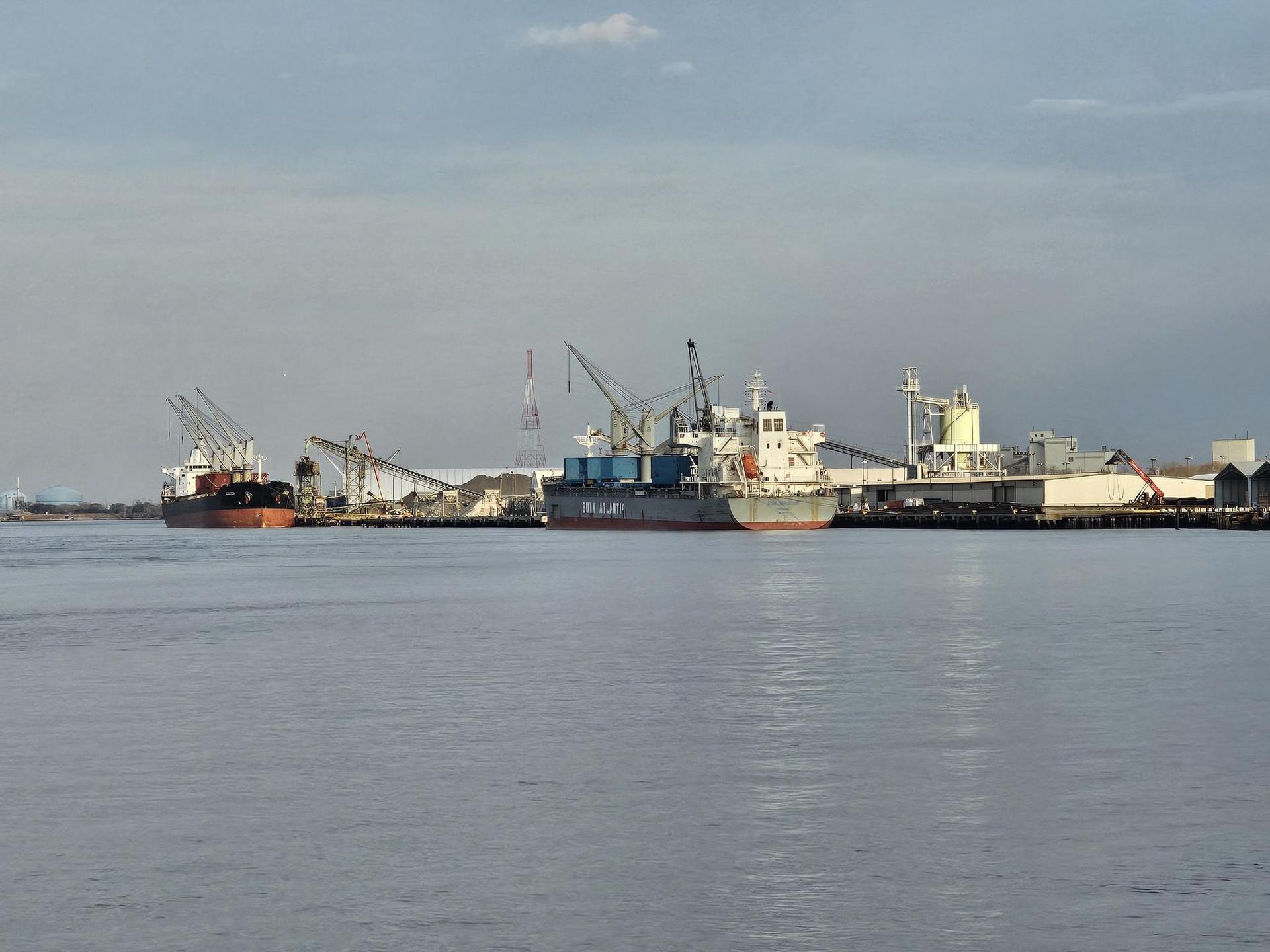 Industrial port with multiple ships and cranes under a cloudy sky.