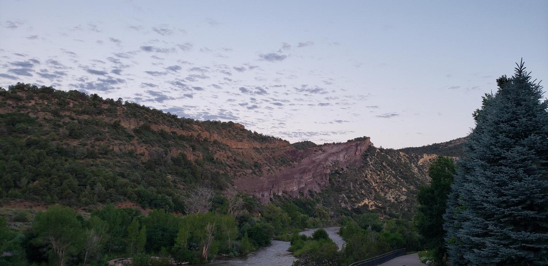 A river winds through a vast, forested mountain landscape at dusk.