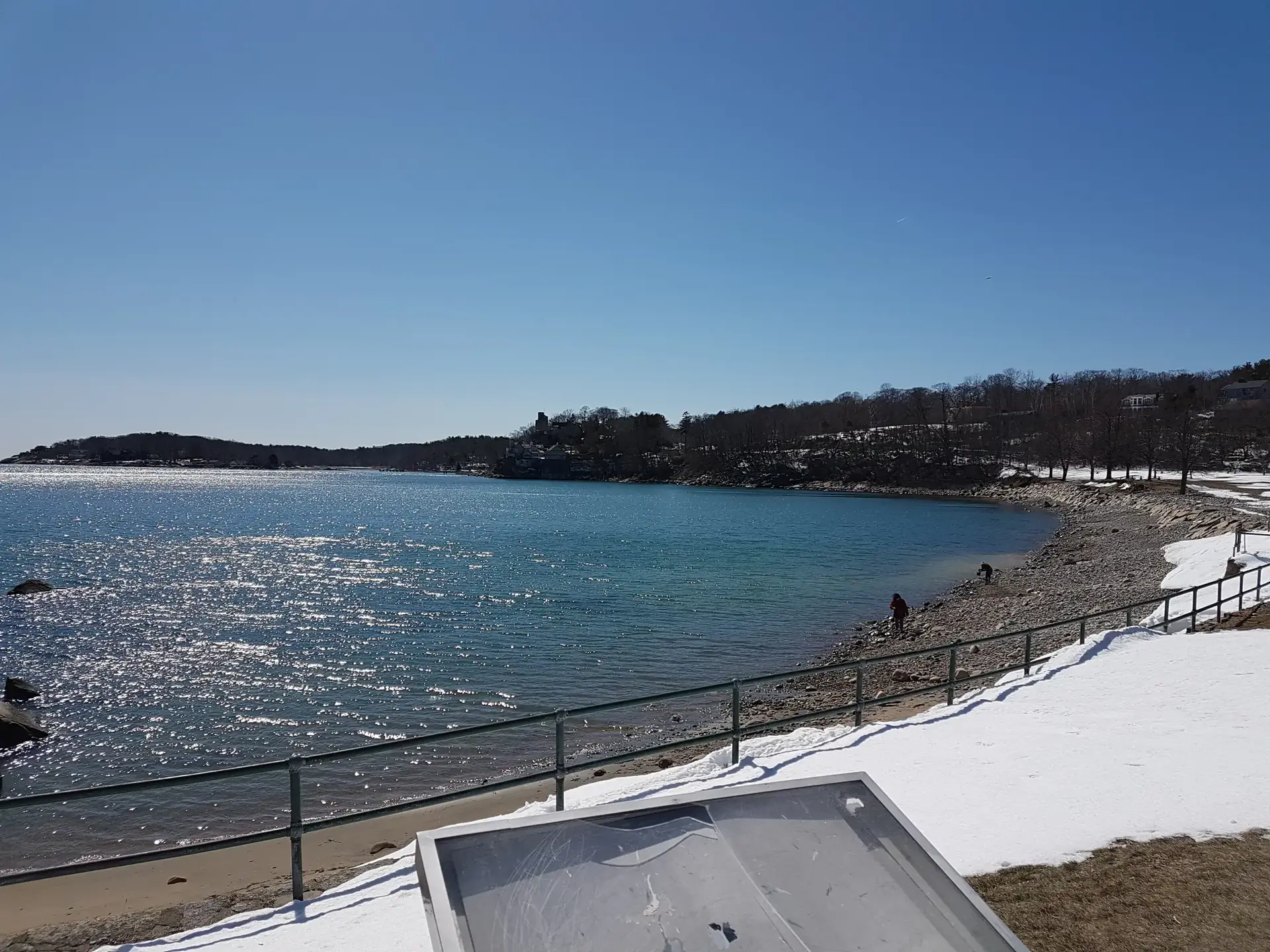 Sunny winter beach scene with sparkling blue water and a person on the shore.