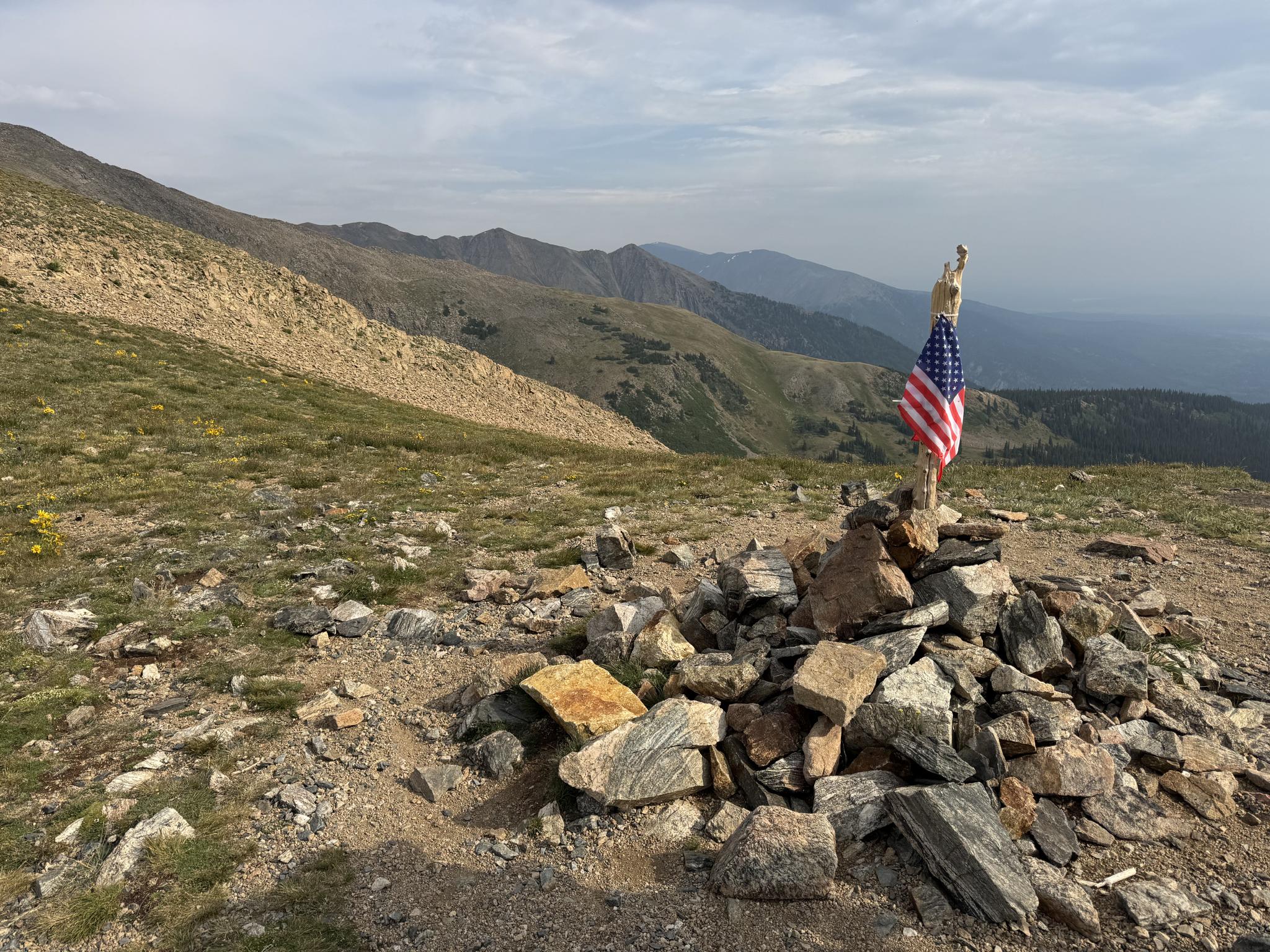 American flag on a rock cairn atop a rocky mountain summit.
