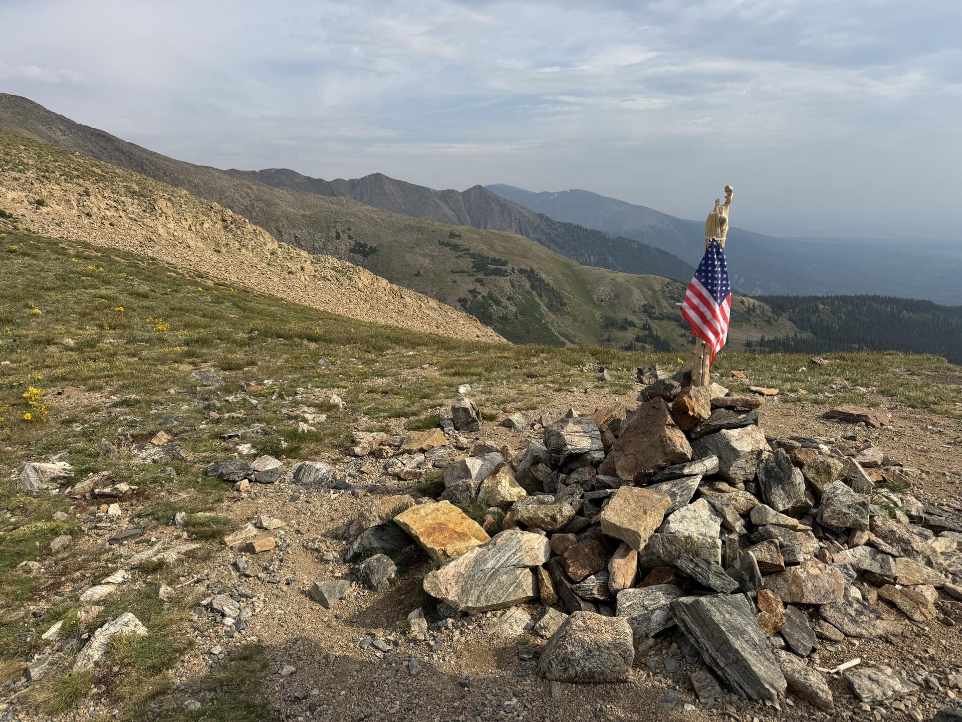 American flag on a rock cairn atop a rocky mountain summit.