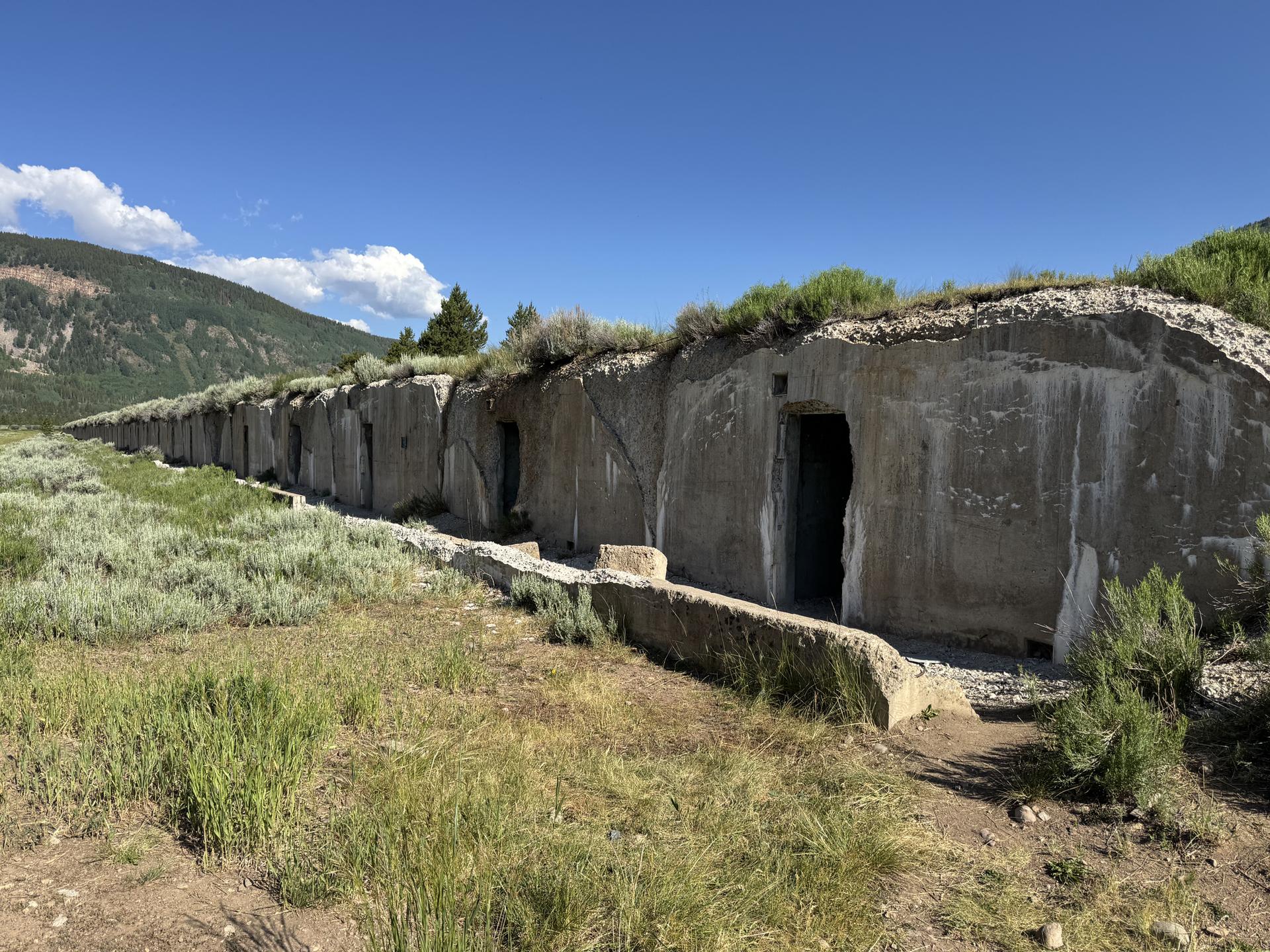 A long concrete structure with multiple arched openings sits in a grassy field.