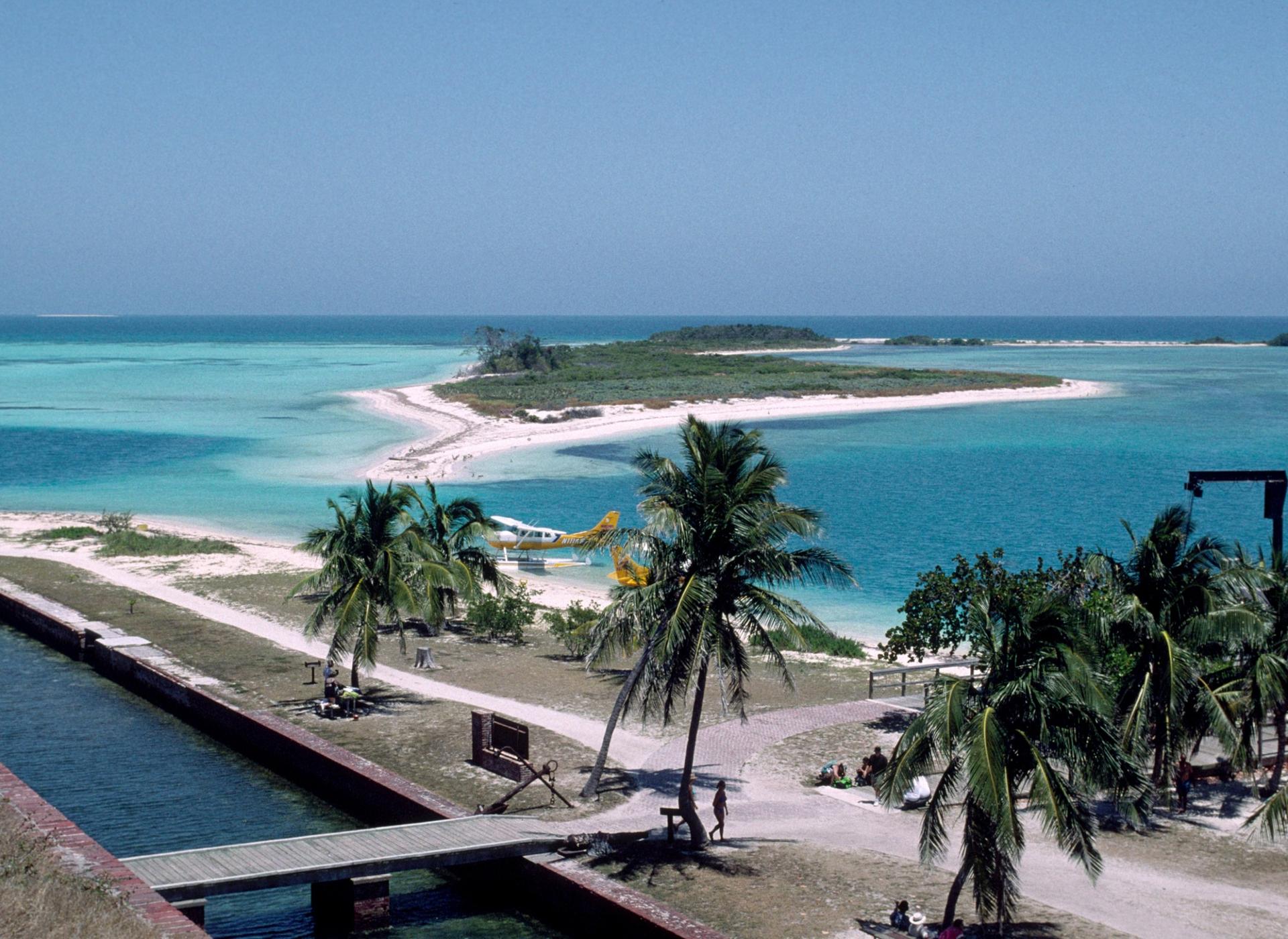 Aerial view of tropical islands, turquoise water, palm trees, and small plane.