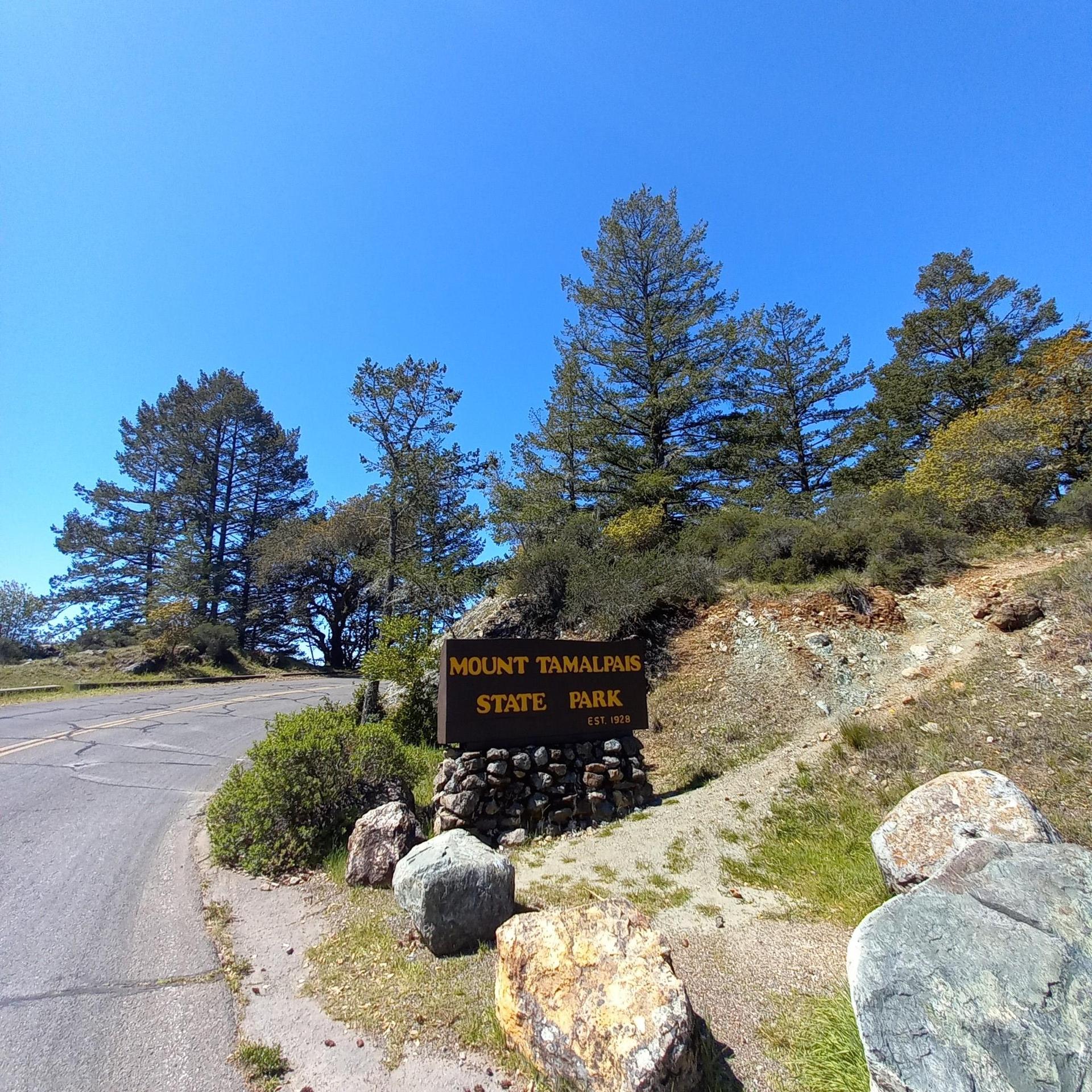 Wooden sign on a rock base next to a road, under a clear sky.