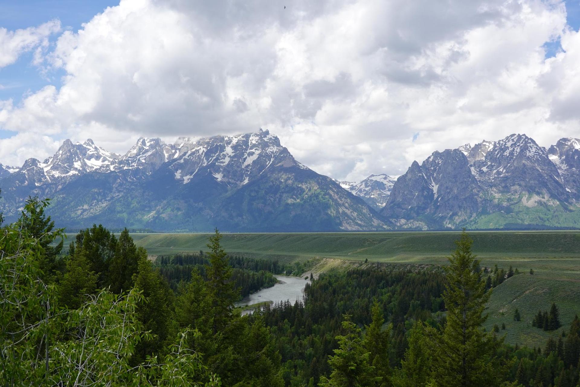 River winding through a valley with snow-capped mountains and cloudy sky.