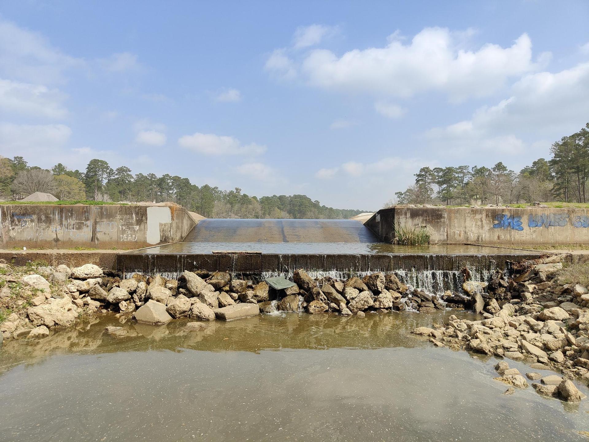 A concrete dam with water cascading over rocks on a bright day.