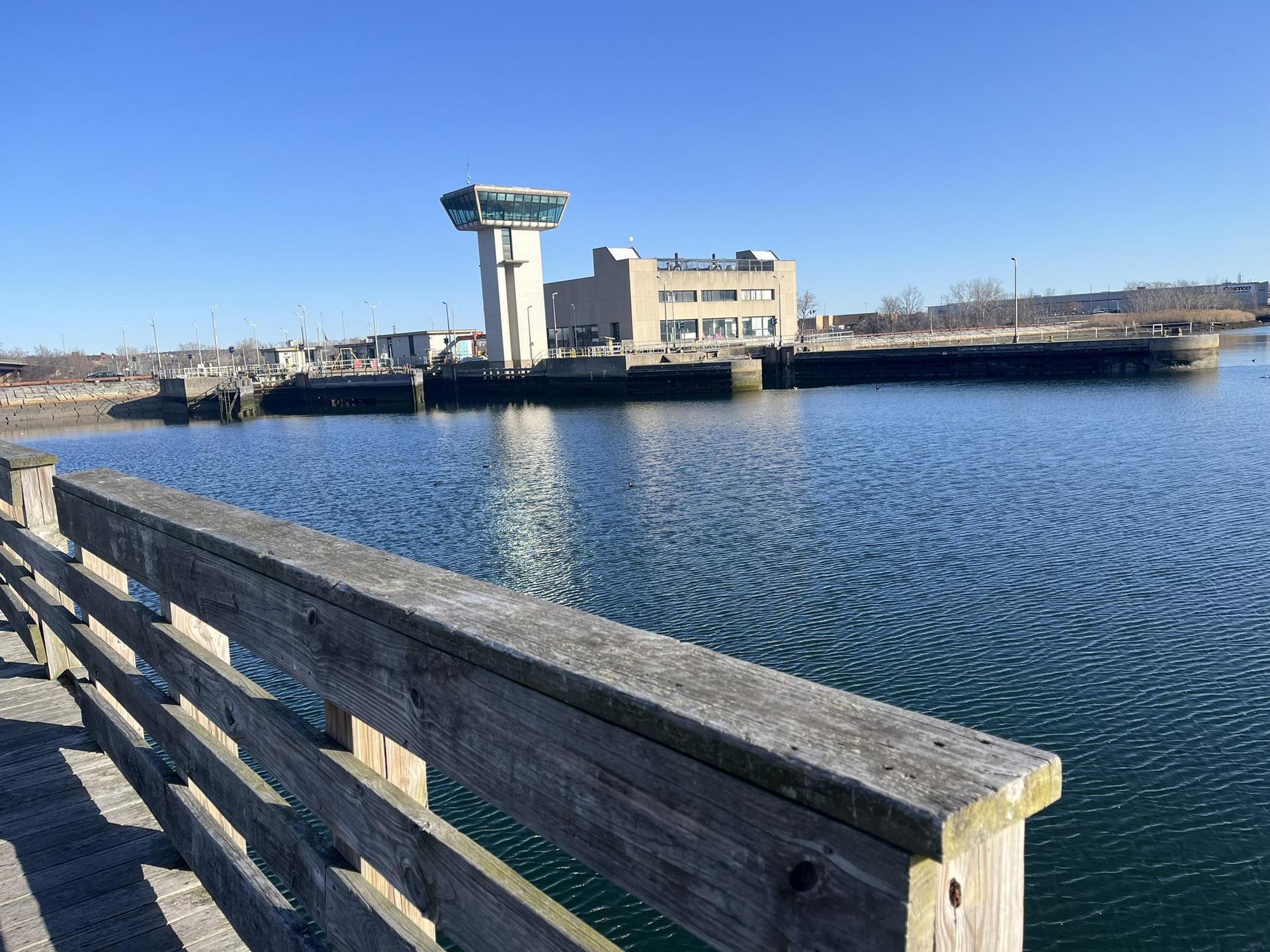 Wooden railing overlooking calm water and a control tower building.