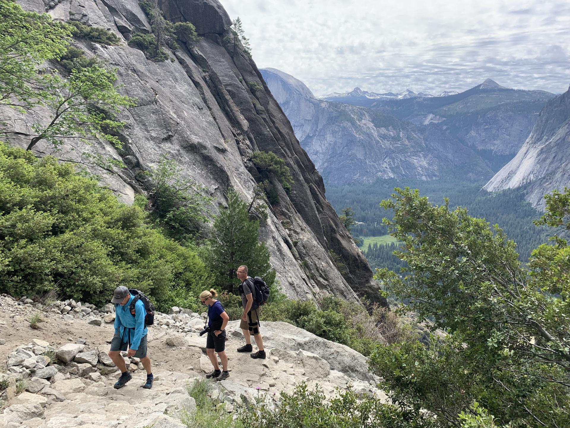 Three hikers on a rocky mountain trail with a valley view.