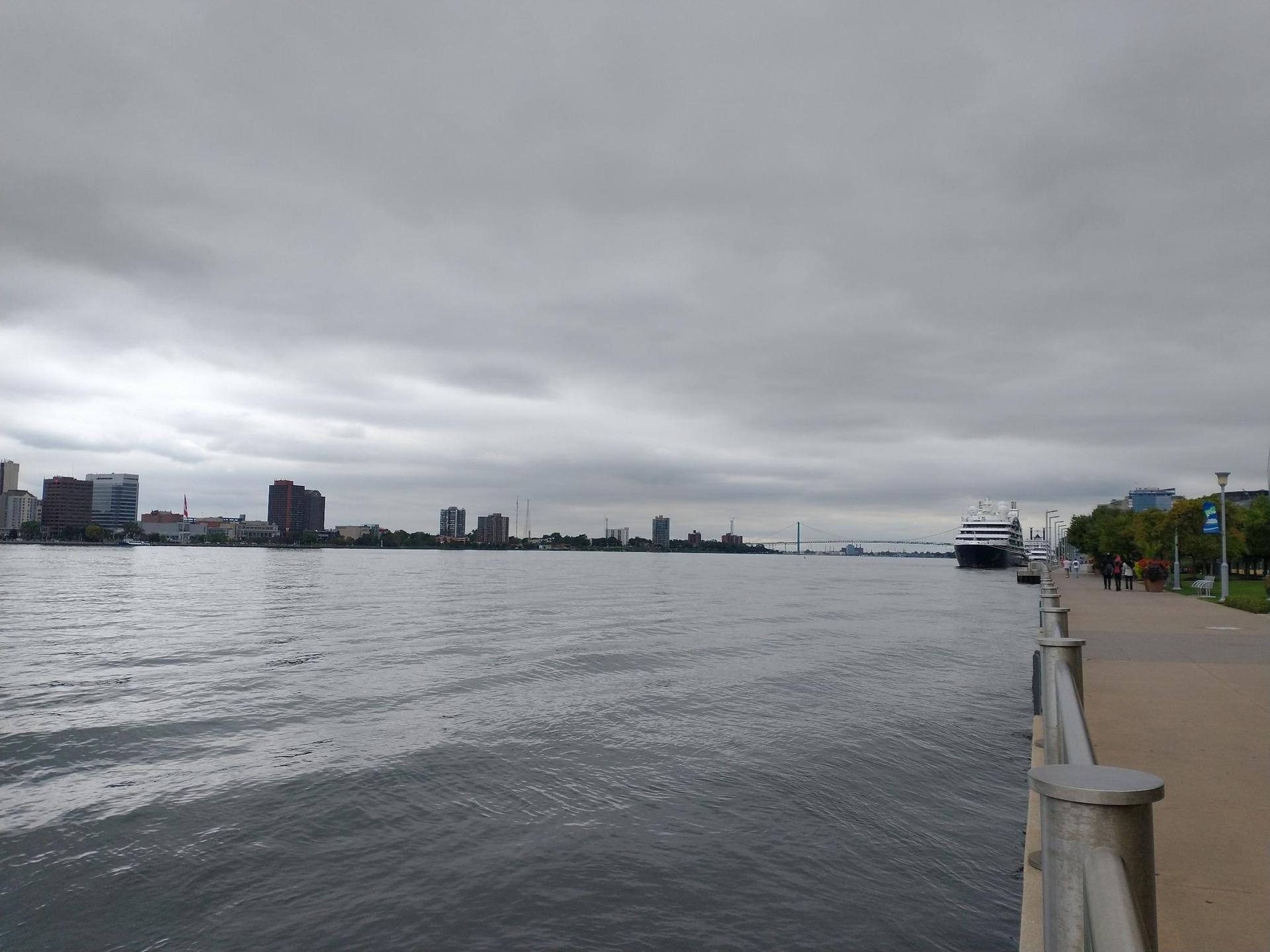 Overcast view of a wide river, city skyline, and a large ship.