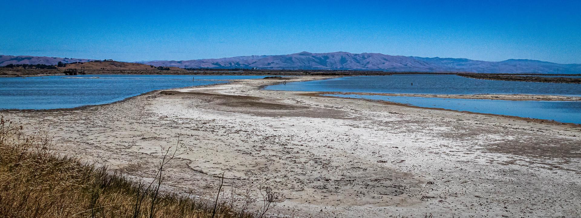 A sandy land bridge separates two bodies of water under a bright sky.