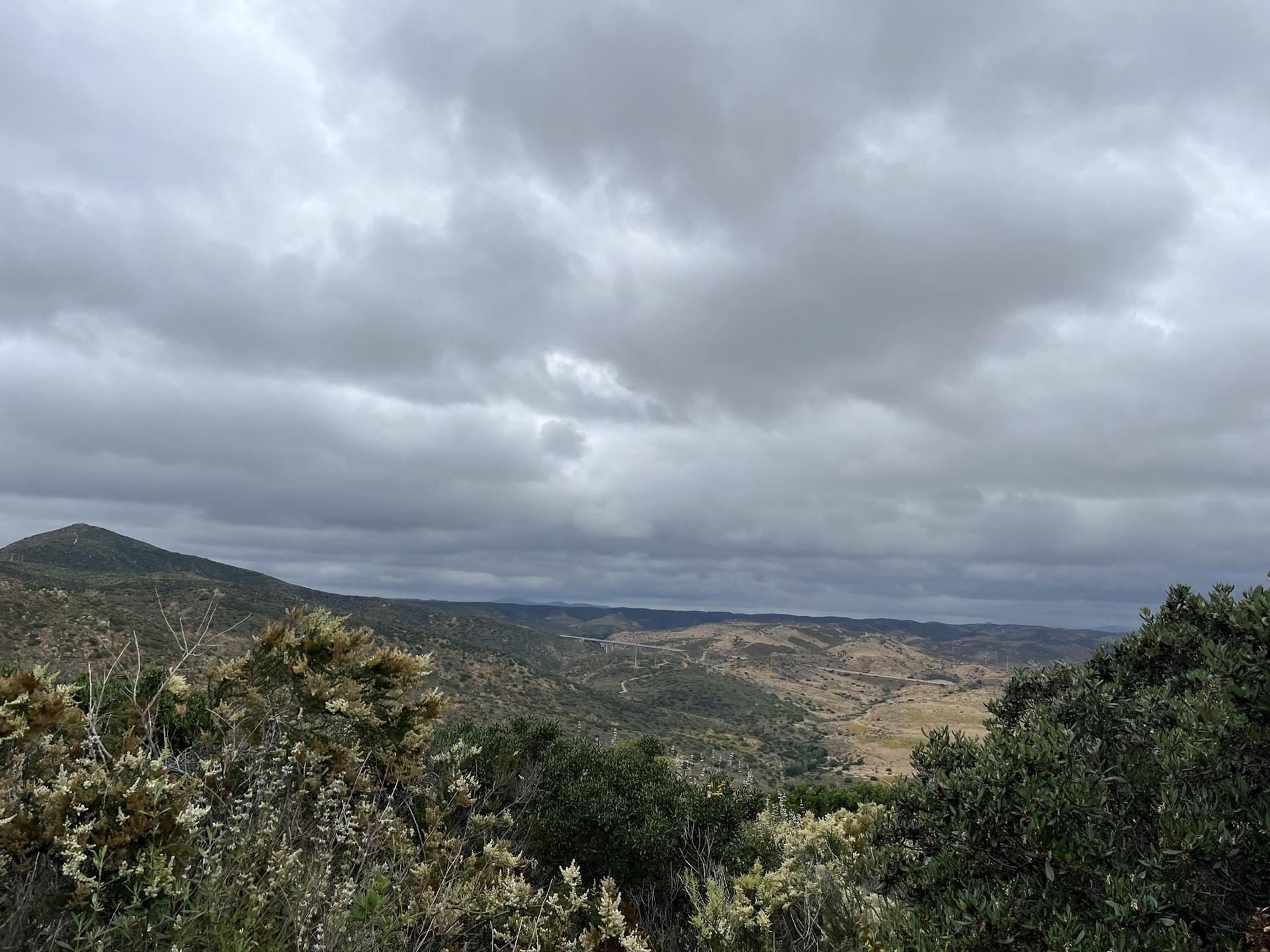 Overcast sky above a vast valley with rolling hills and green foliage.