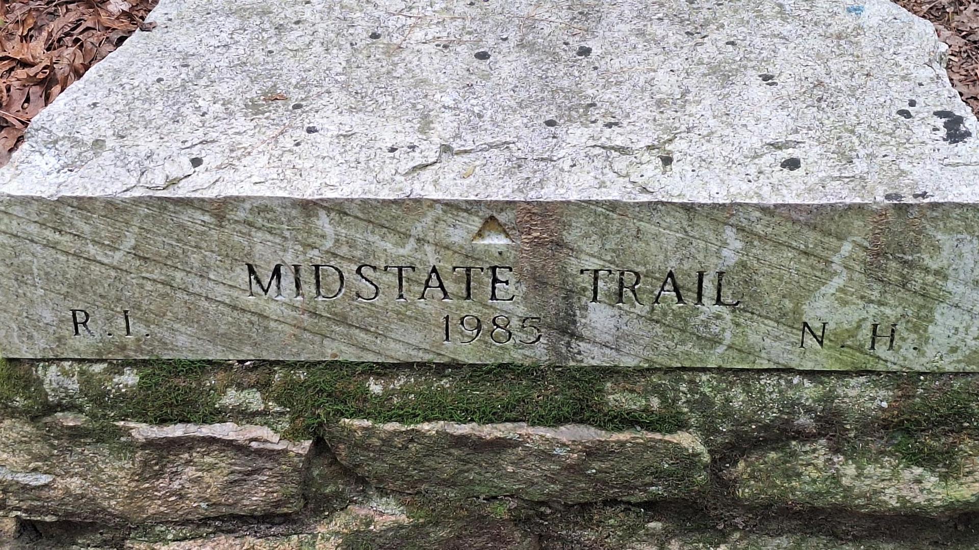 Close-up of a weathered stone trail marker with carved text and moss.