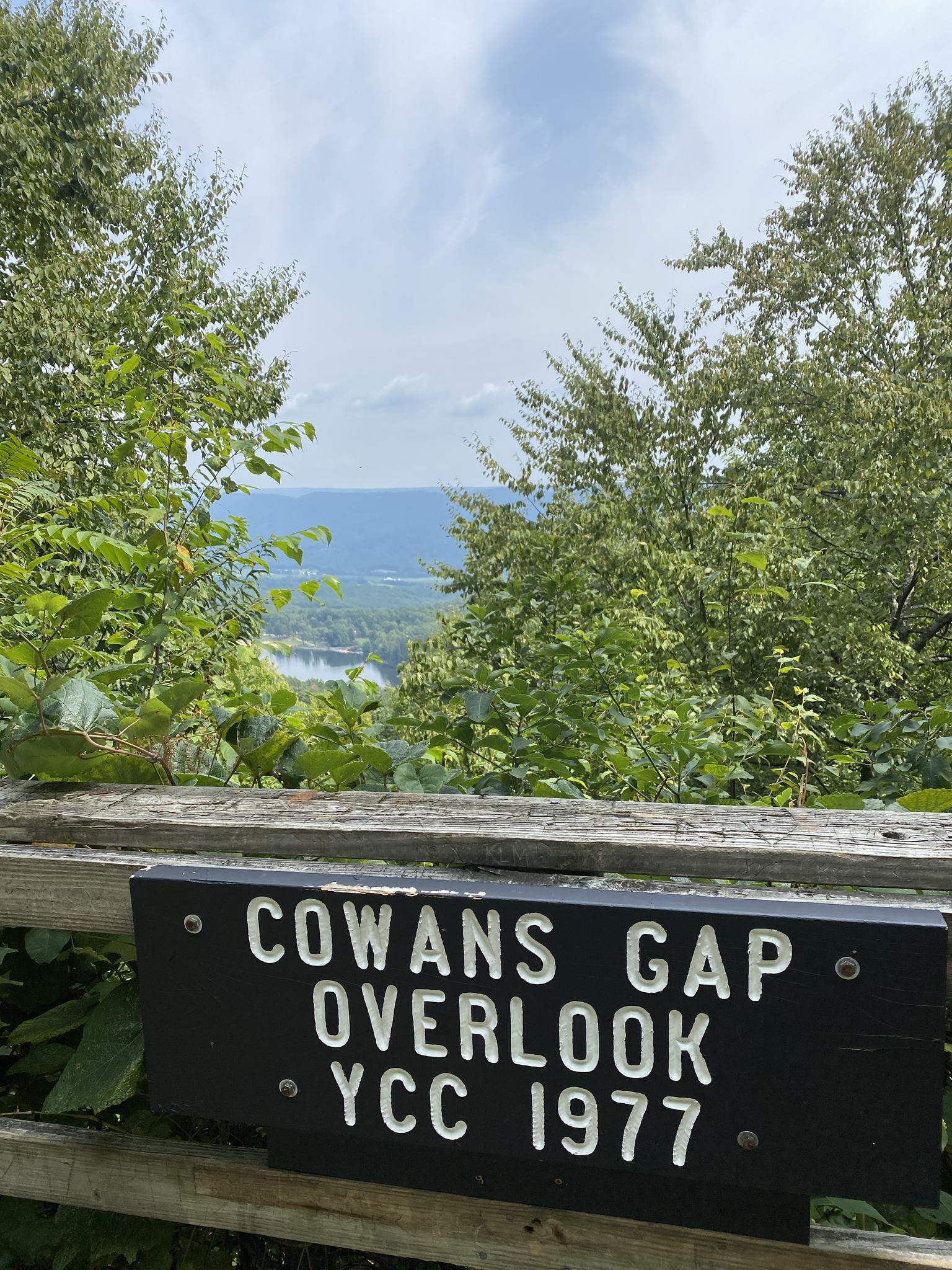 A wooden sign in front of a scenic overlook with a distant valley view.